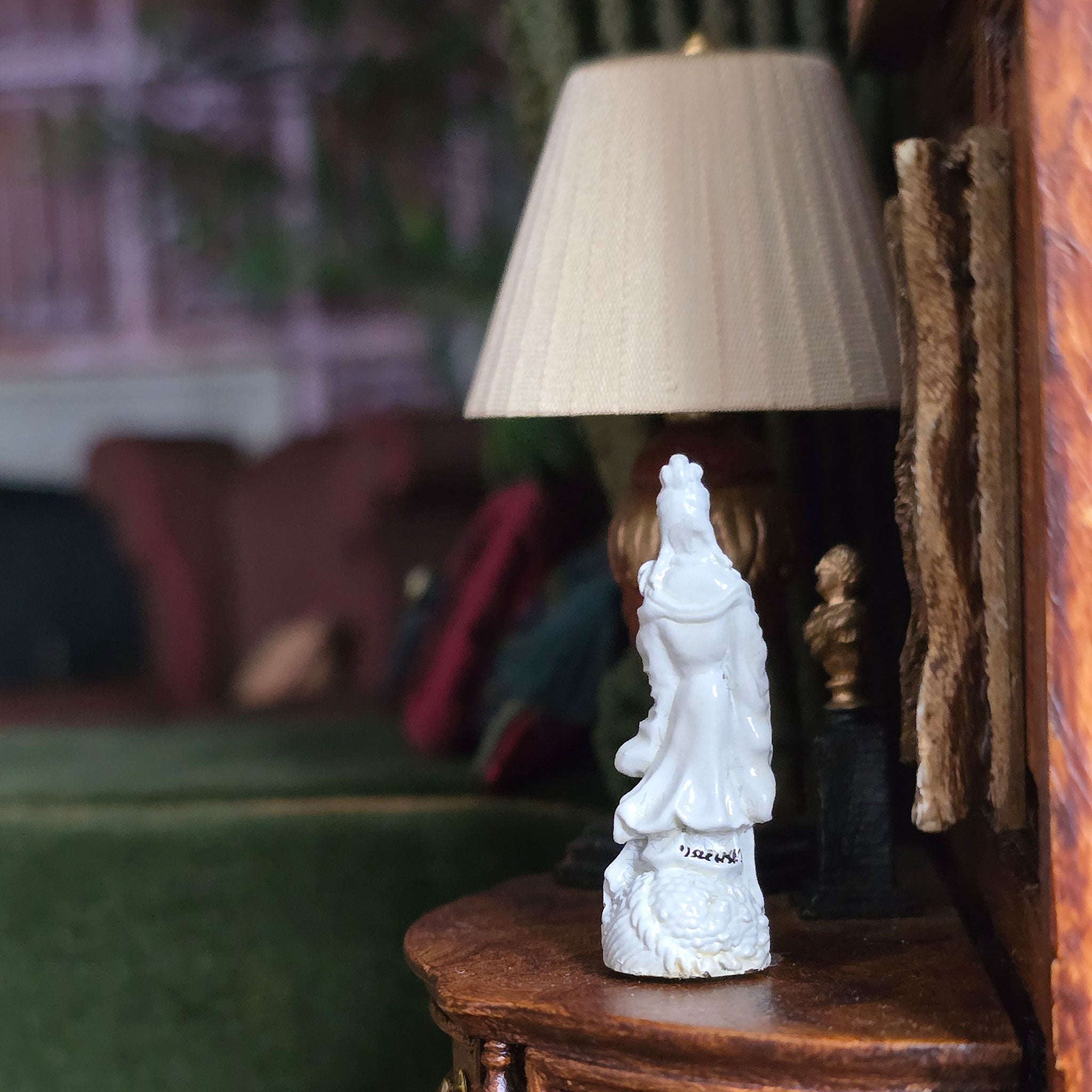 White statue of a figure on a wooden shelf with a lamp in the background