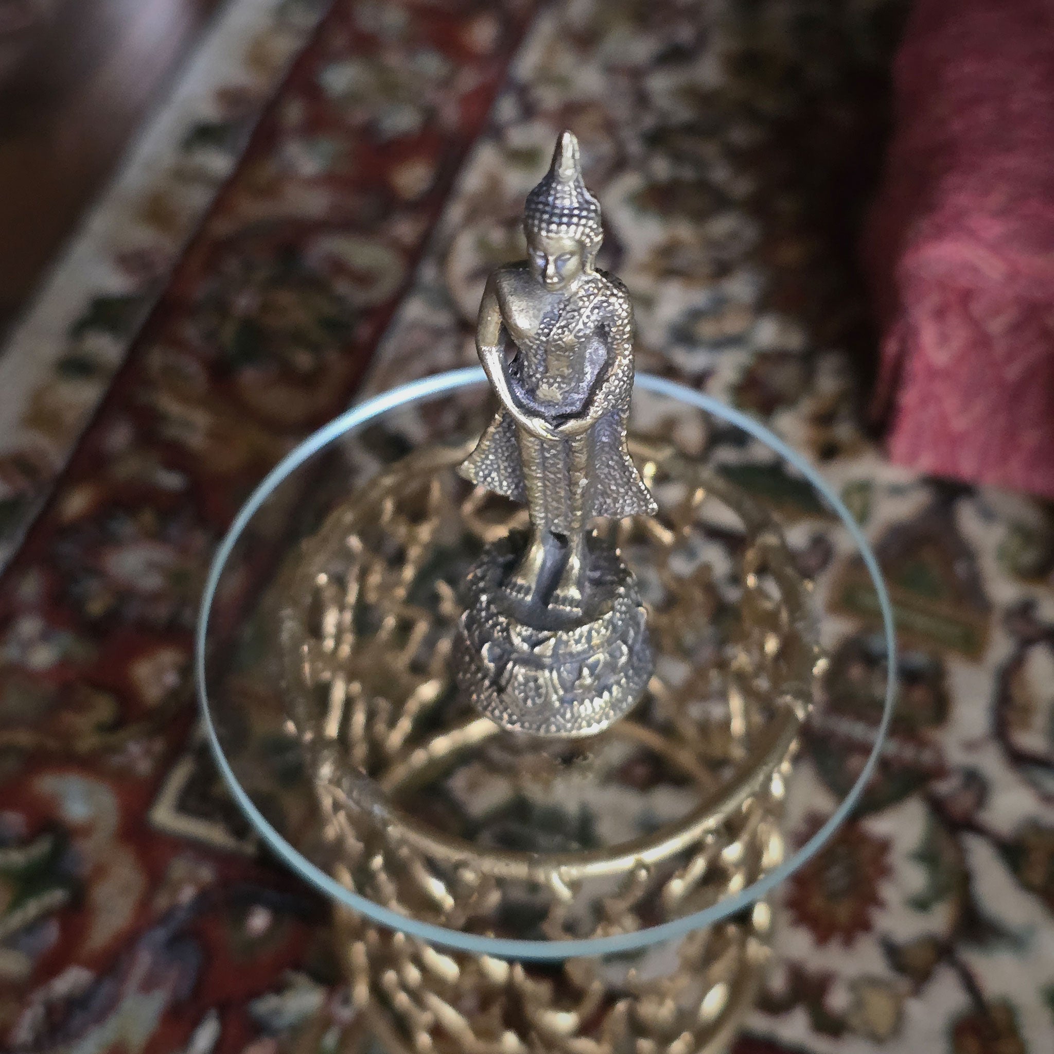 Small Buddha statue on a decorative stand with a patterned fabric background