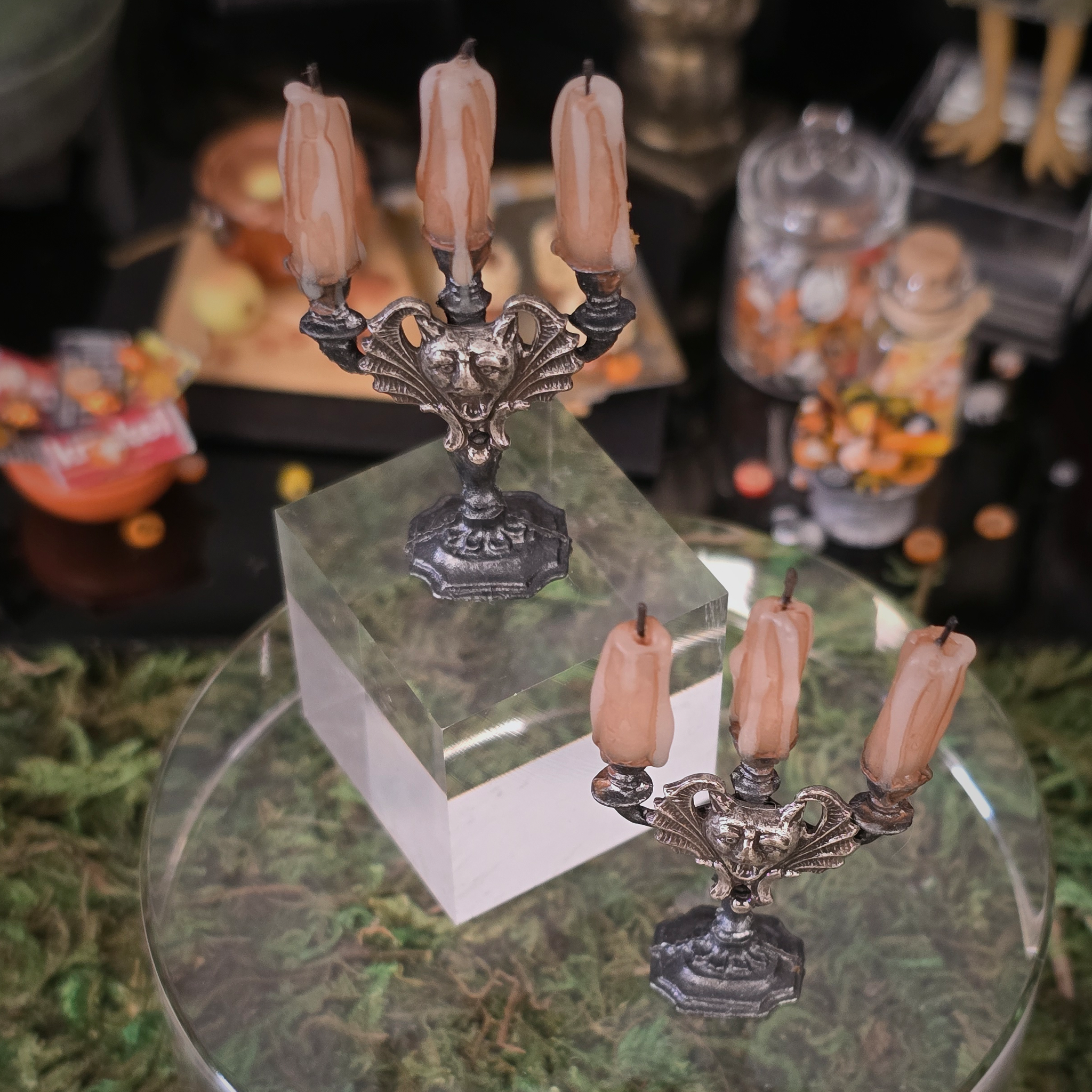 Decorative candle holders with candles on a glass table with Halloween-themed decorations in the background.