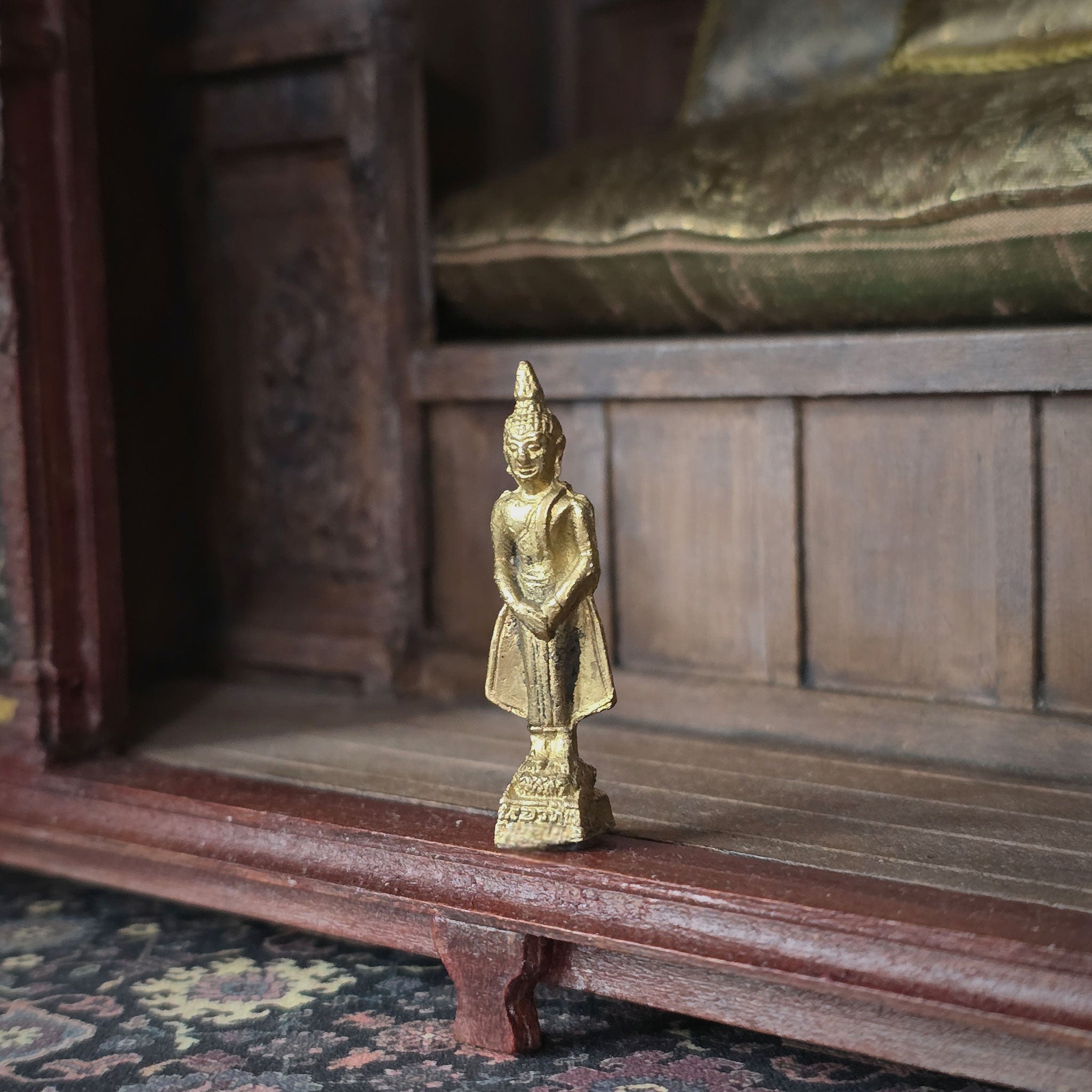 Gold Buddha statue on a wooden shelf with a wooden cabinet in the background