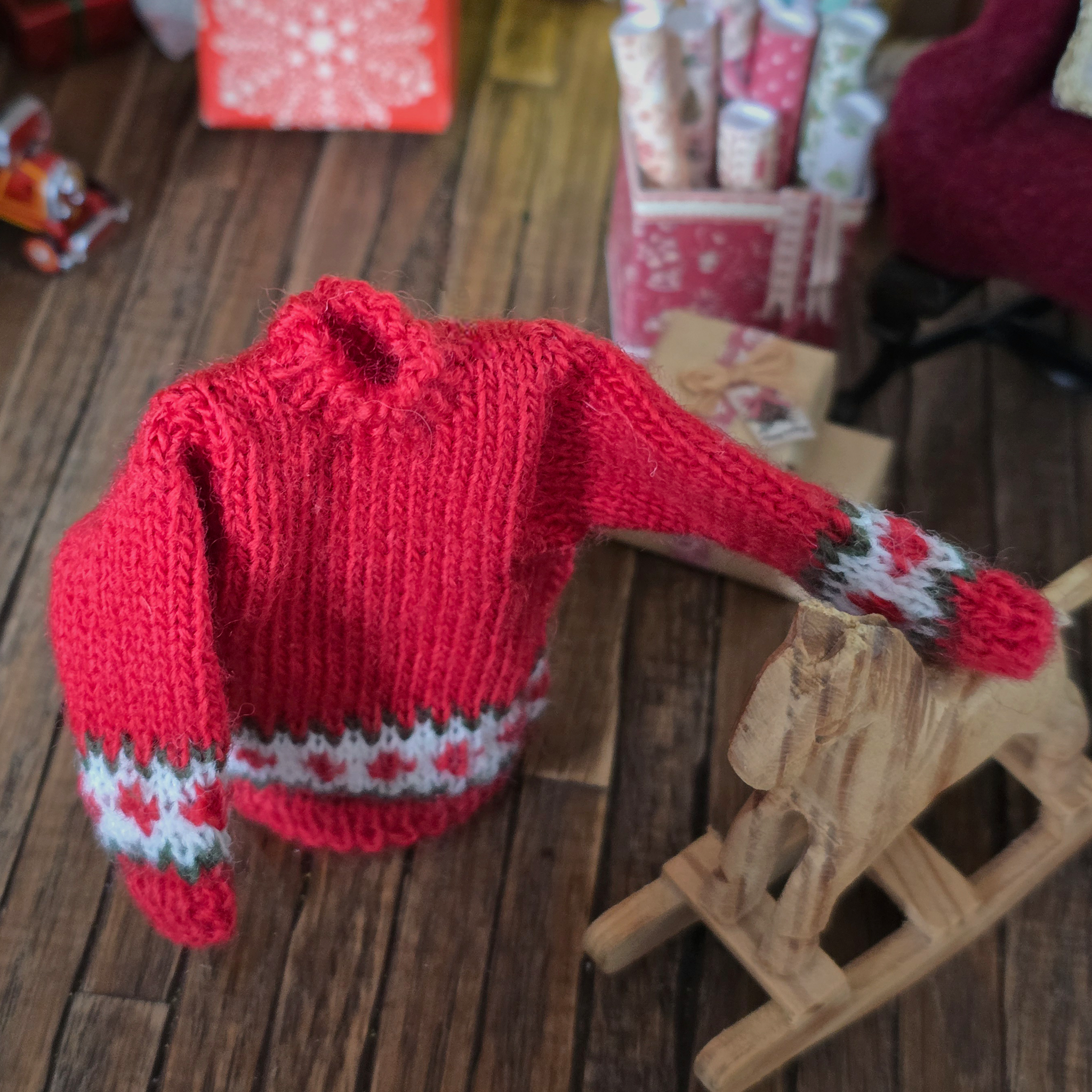 Red knitted sweater with white and green patterns on a wooden surface, close up detail, Dollhouse miniature 