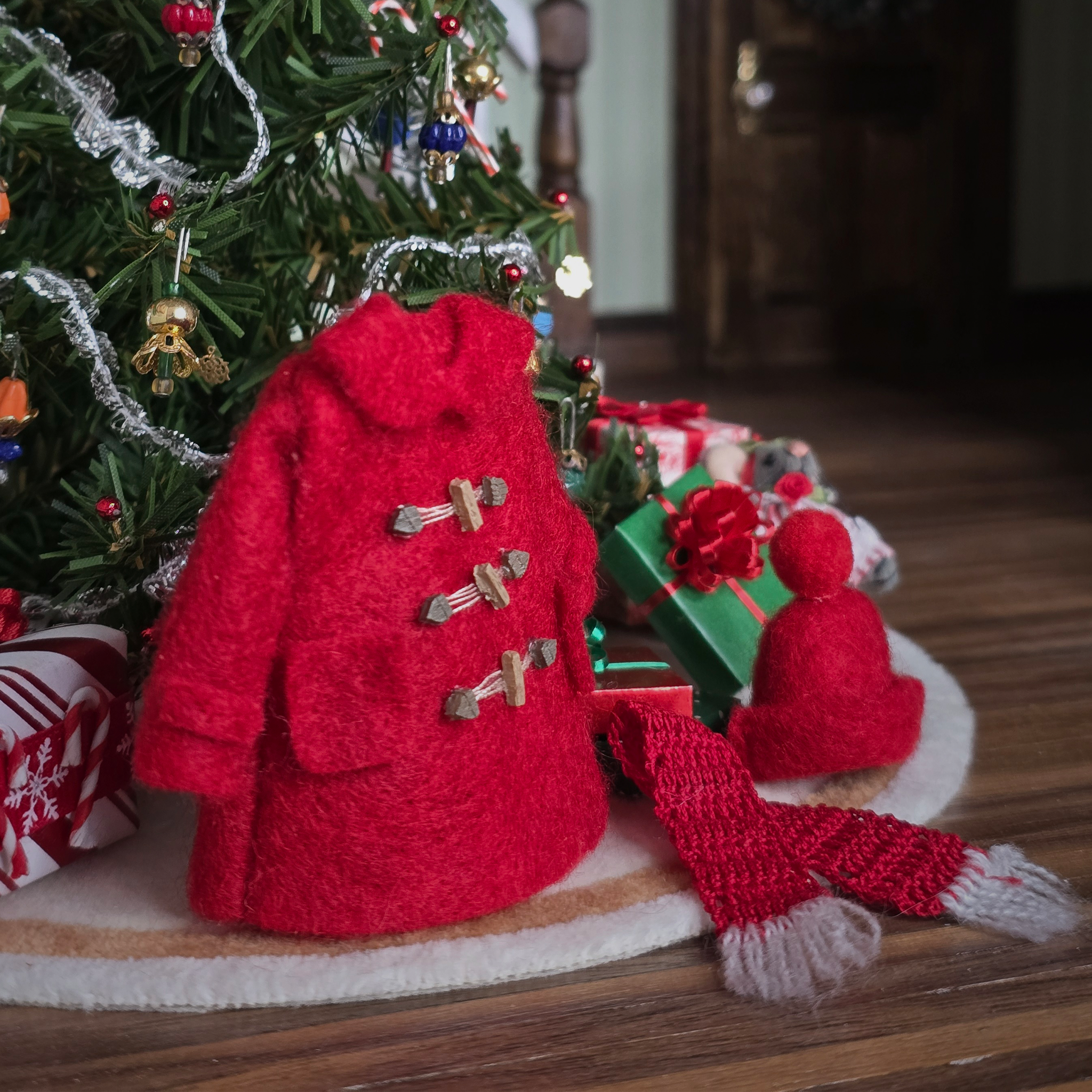 Knitted red coat with a matching hat and scarf in front of a decorated Christmas tree.