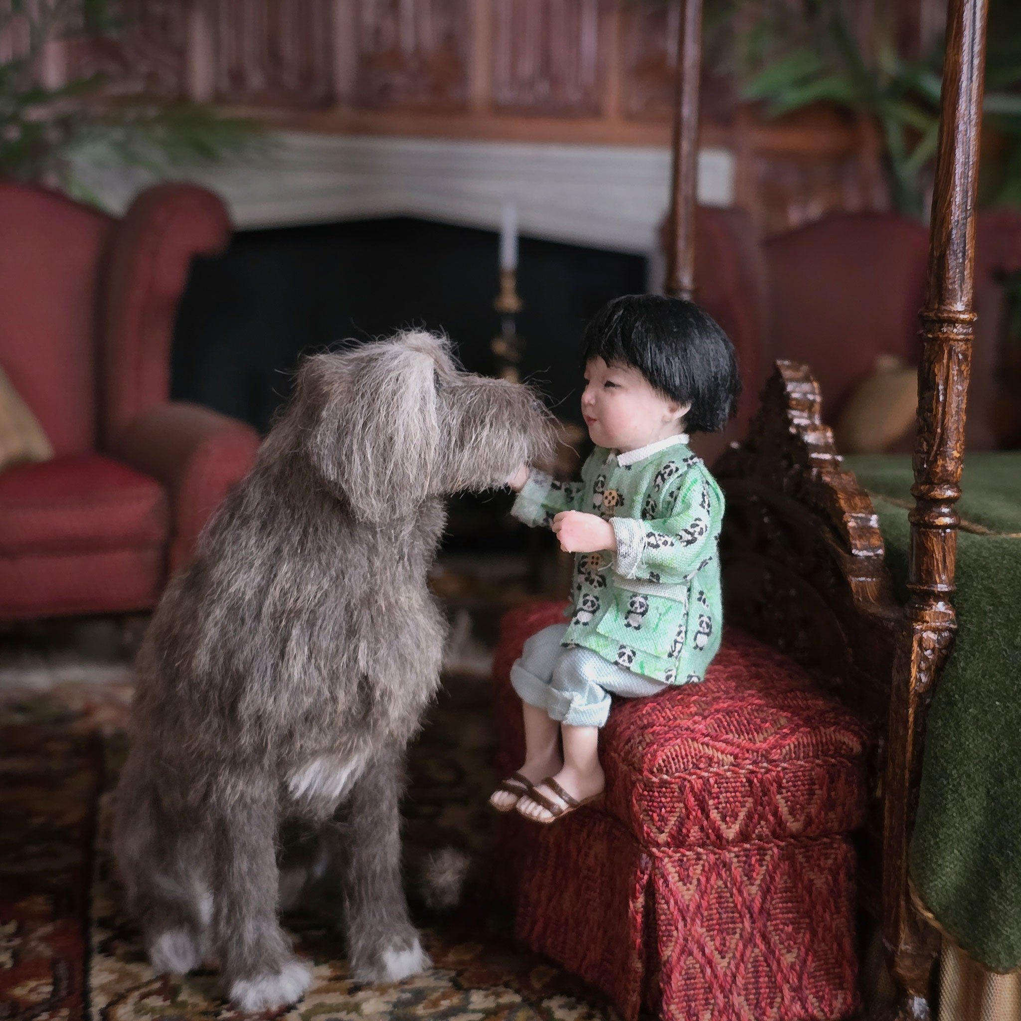 Child in a green panda print shirt sitting on a red chair next to a large dog in a cozy room.