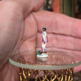 Load image into Gallery viewer, Small figurine of a person in traditional attire held in a hand on a clear stand.

