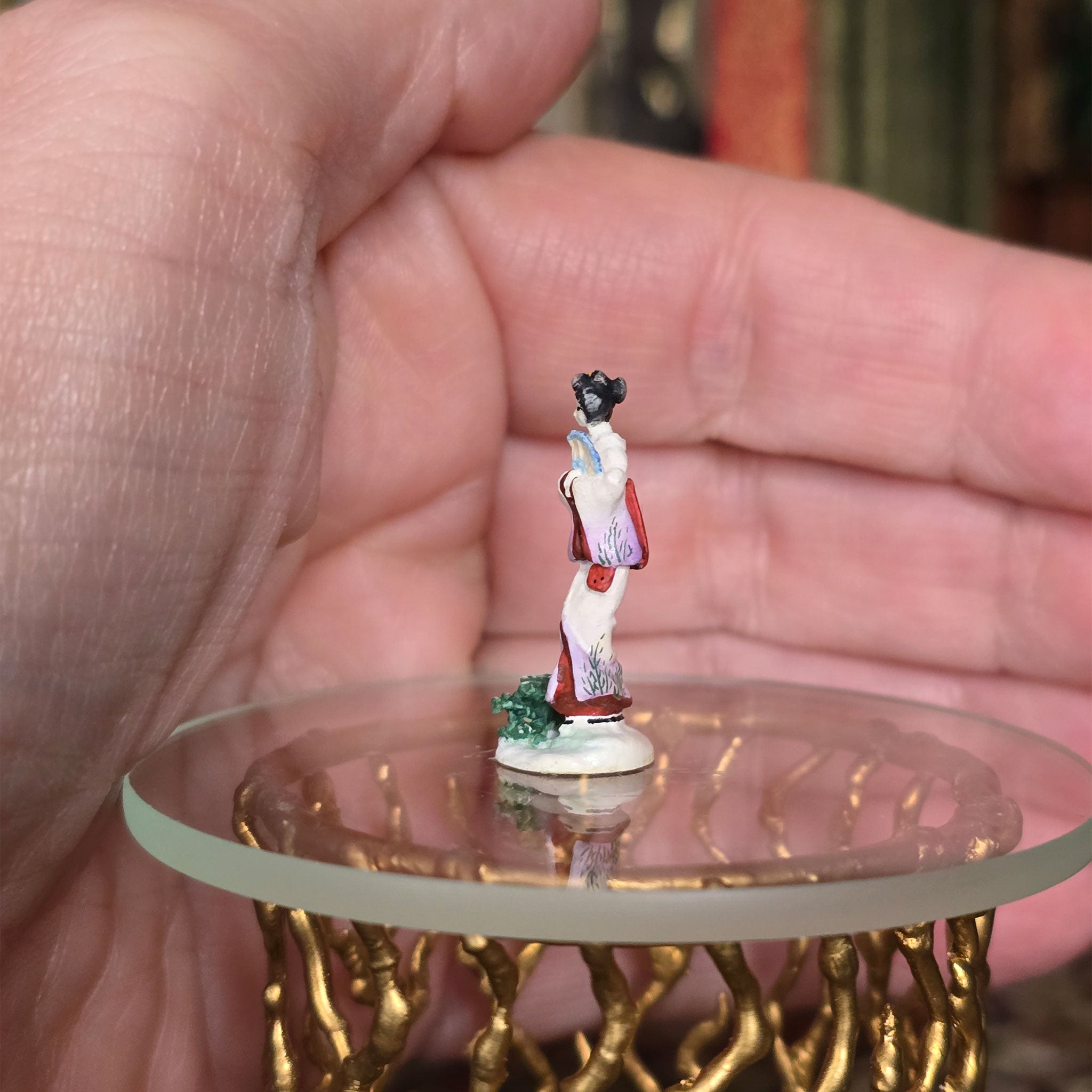 Small figurine of a person in traditional attire held in a hand on a clear stand.