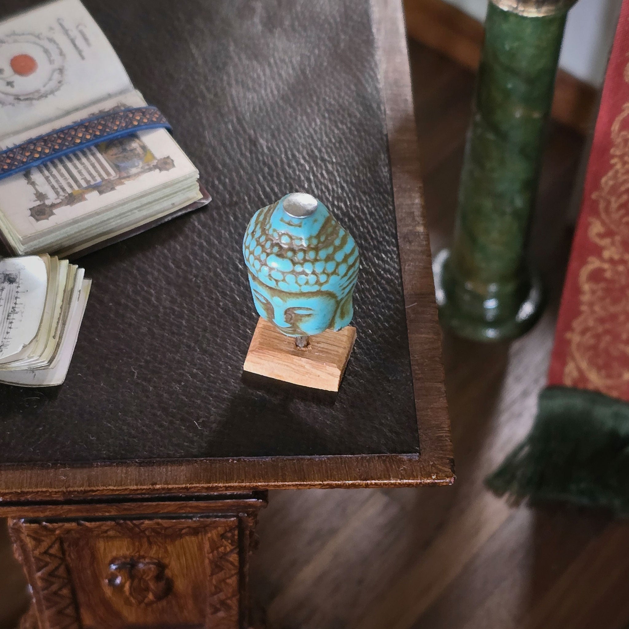 Small turquoise ceramic vase on a wooden stand with books and a green column in the background. Miniature