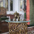 Load image into Gallery viewer, Gold elephant figurine on a glass-top table with a textured base in a blurred indoor setting
