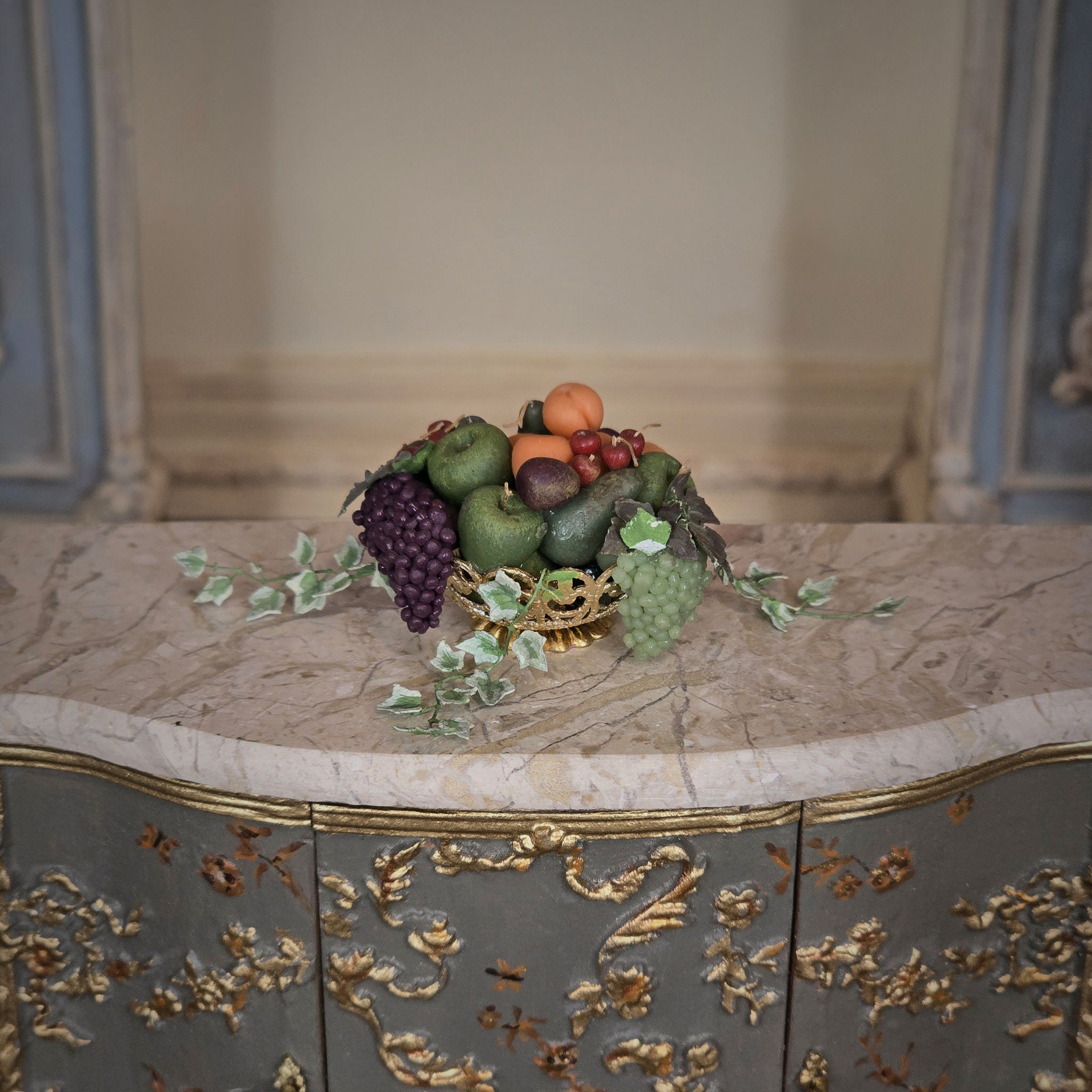Decorative miniature dollhouse fruit bowl on a marble surface with ornate furniture in the background