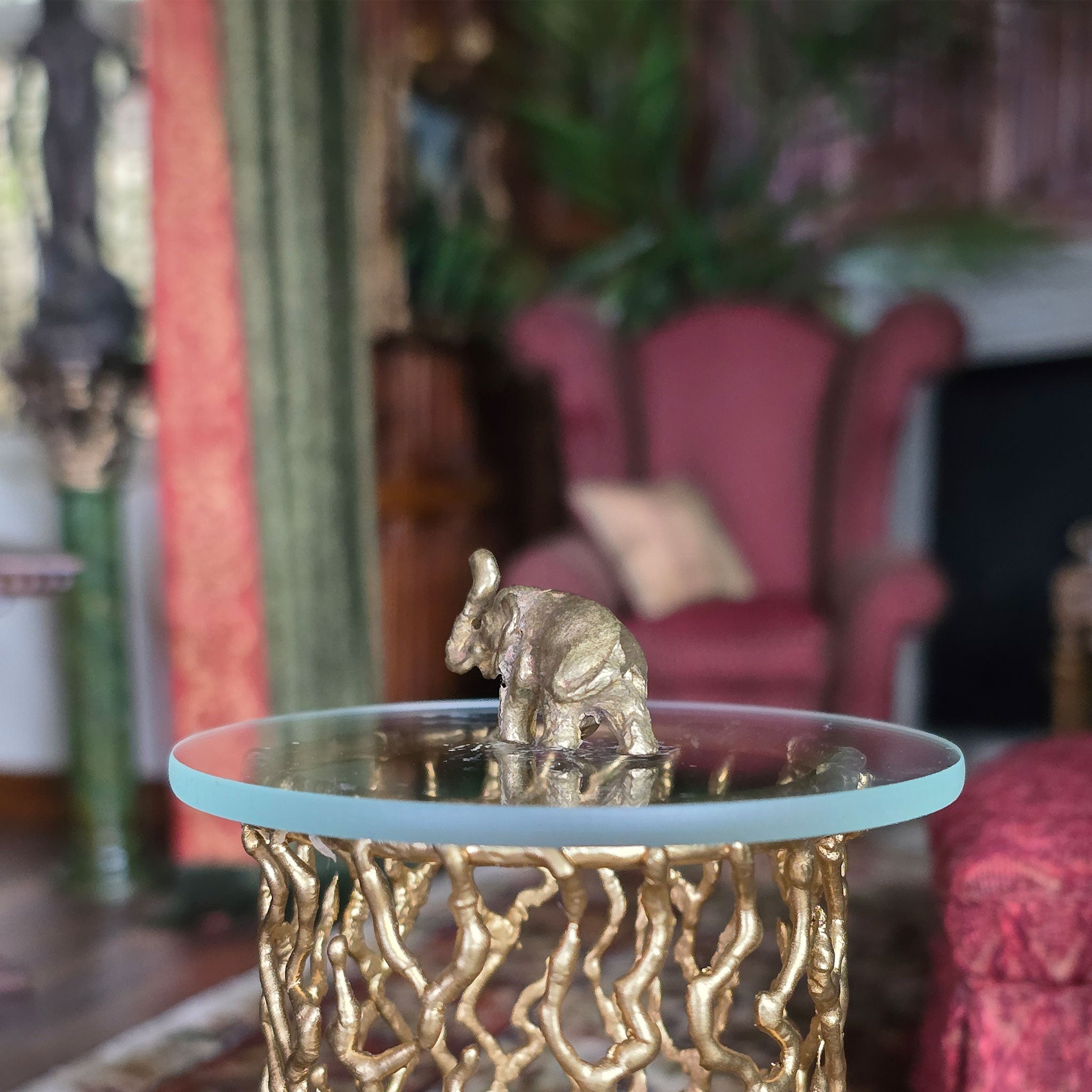 Decorative table with a gold elephant sculpture in a room with pink chairs and a plant.