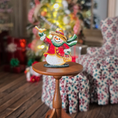 Load image into Gallery viewer, Decorative snowman figurine on a small wooden table with a blurred Christmas tree and chair in the background.
