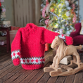 Load image into Gallery viewer, Dollhouse miniature Red knitted sweater with white and green patterns on the sleeves and hem, in front of a decorated Christmas tree.
