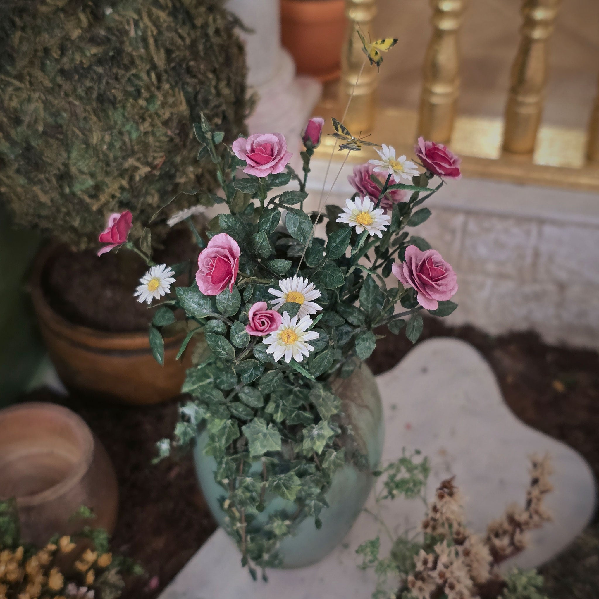 Bouquet of pink roses and white daisies in a planter on a decorative surface.