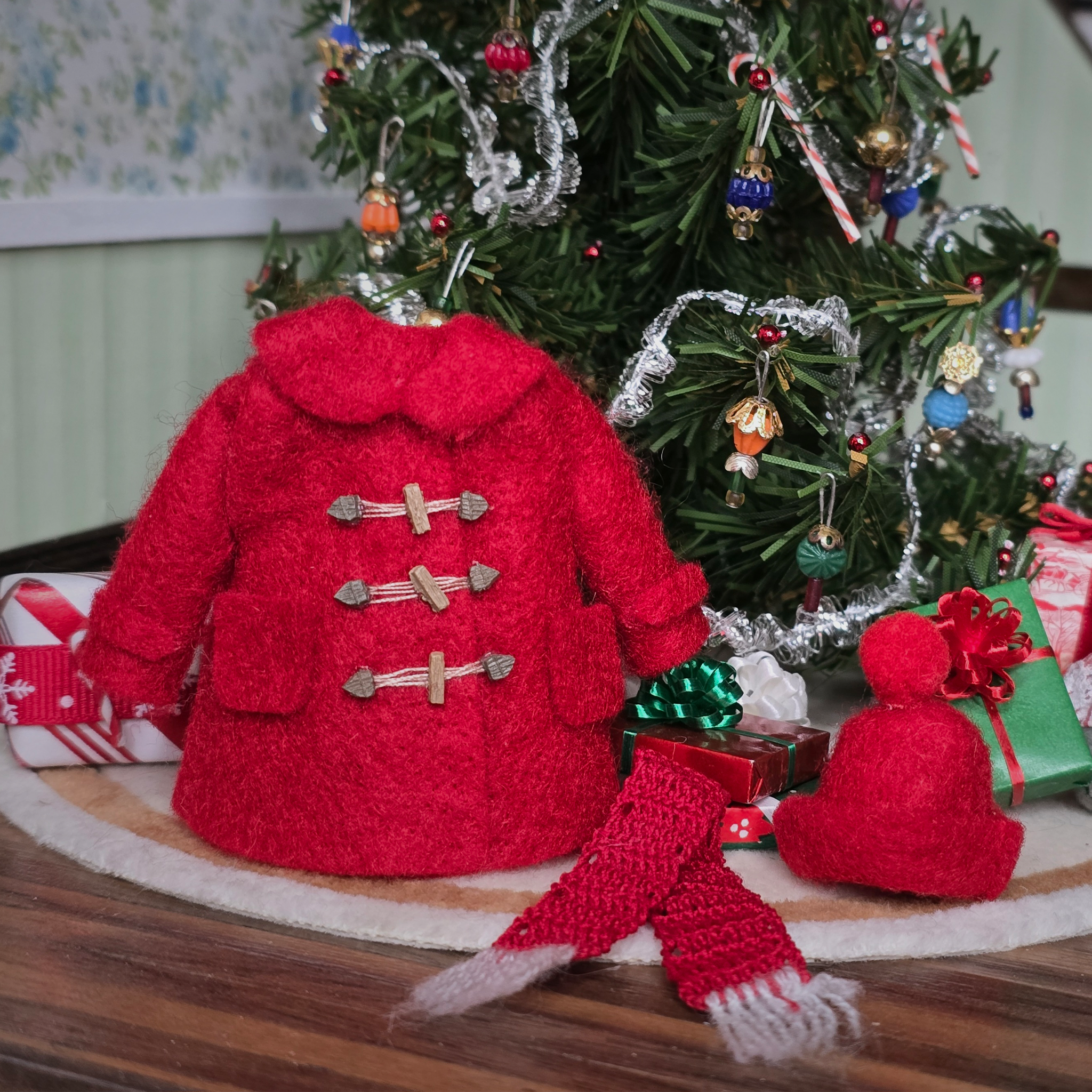 Dollhouse miniature Red knitted coat, scarf, and hat on a Christmas tree with decorations and presents.