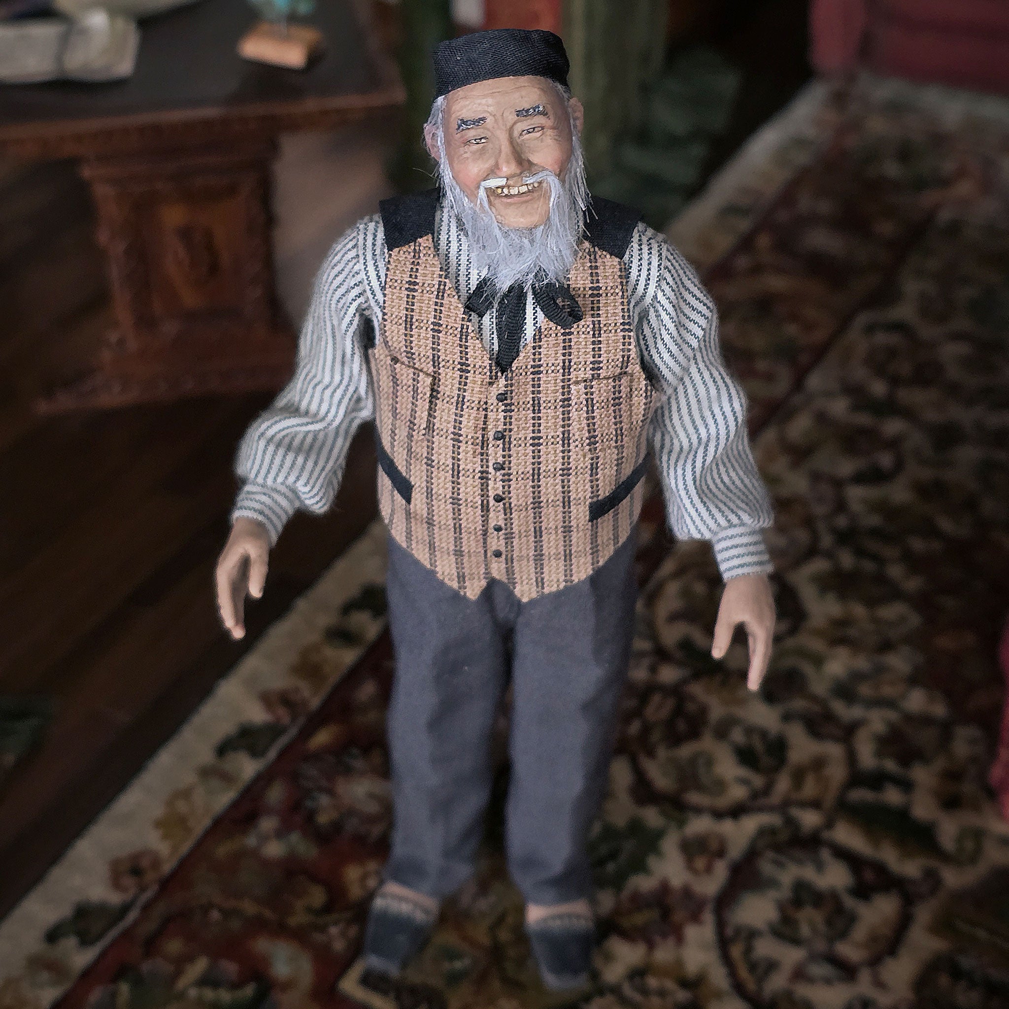 Vintage-style Asian clay dollhouse doll - an elderly man with a beard on a patterned rug.