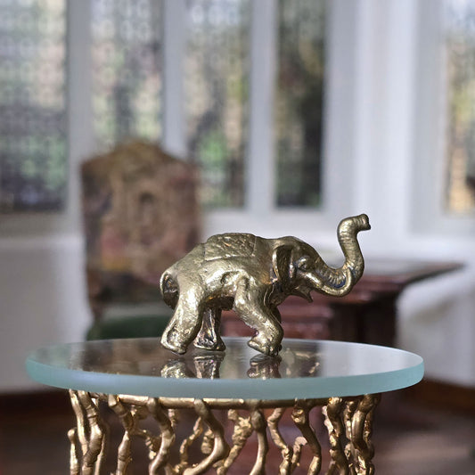 Gold elephant figurine on a round glass table with a blurred indoor background