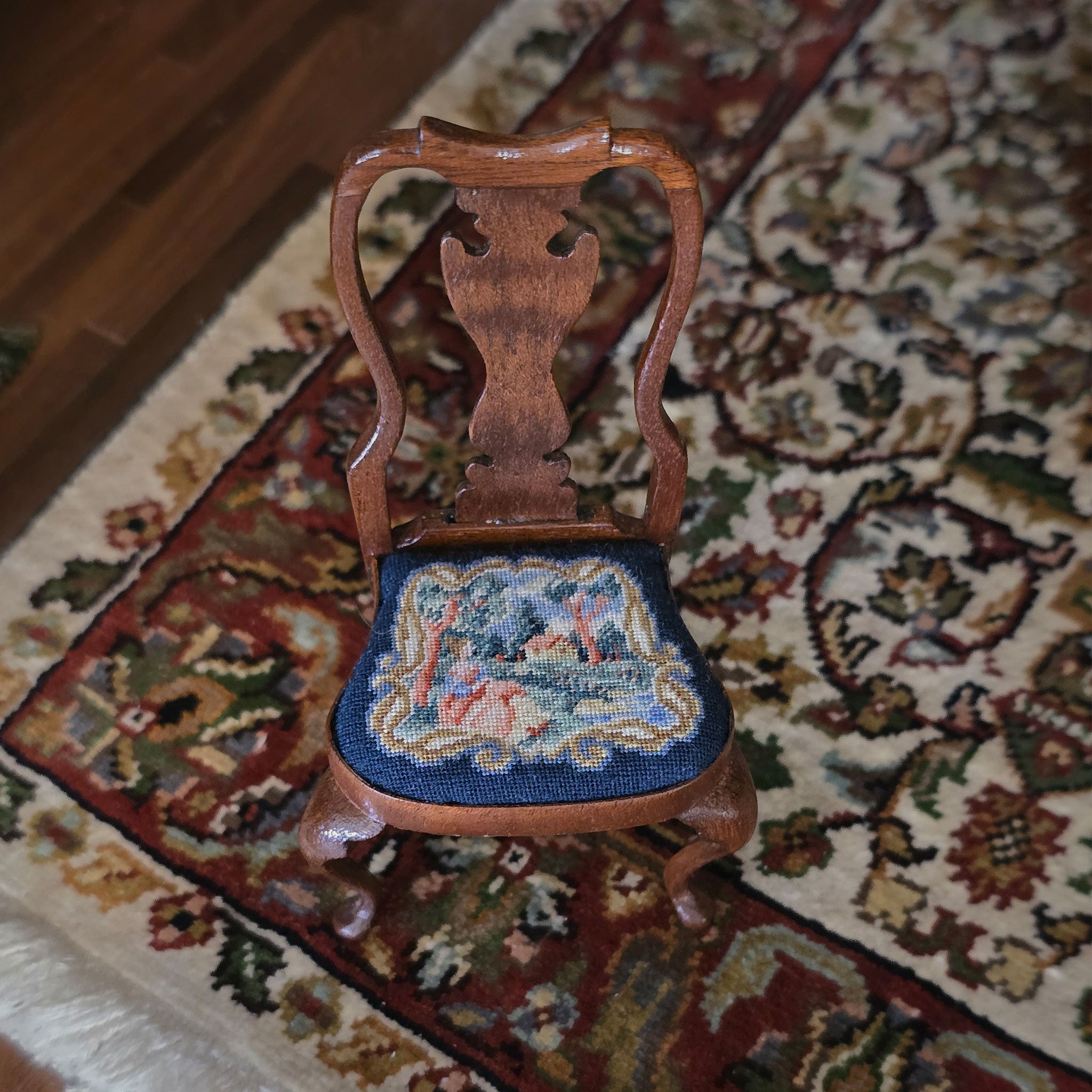 Wooden chair with a needlepoint seat on a patterned rug