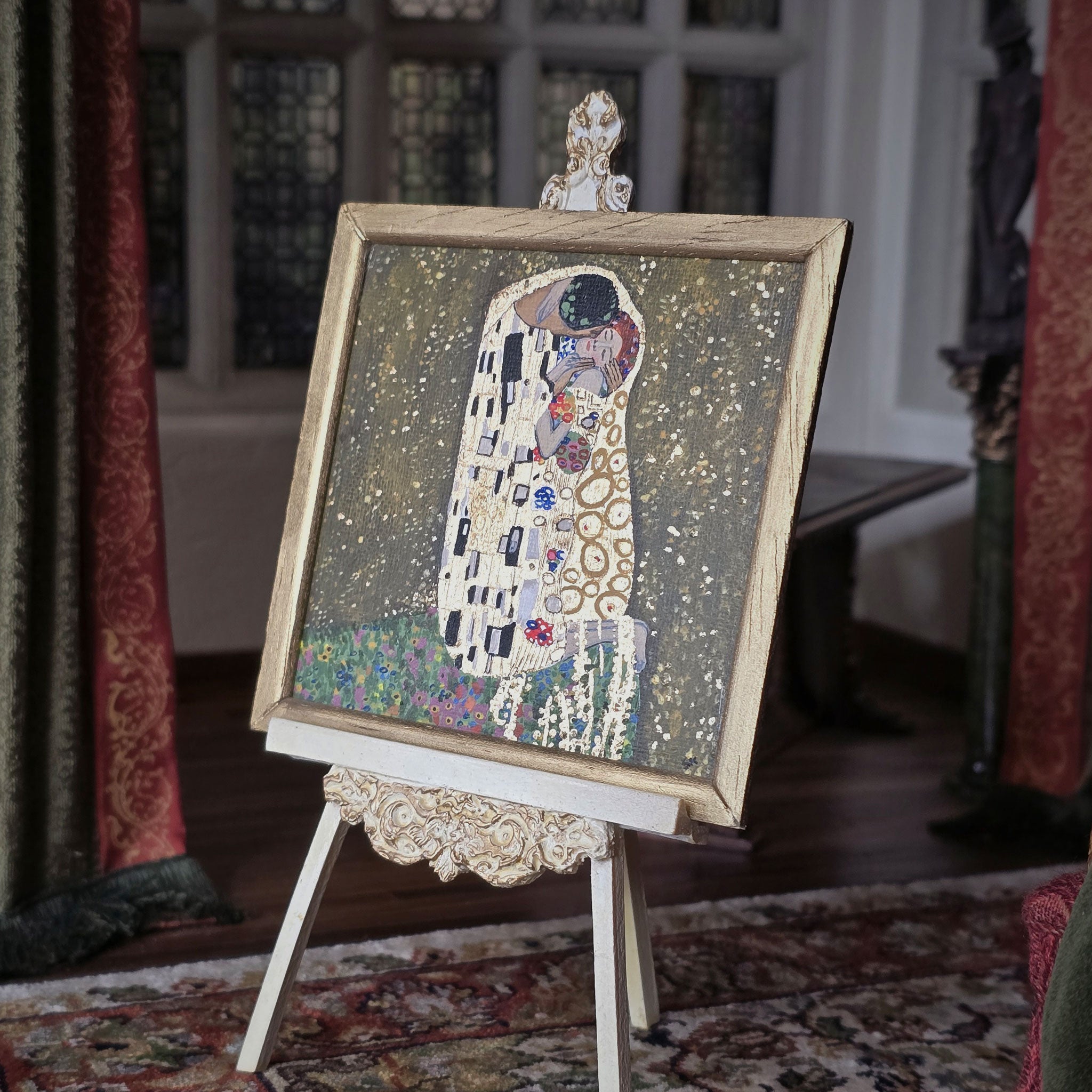 Artistic depiction of 'The Kiss' by Gustav Klimt in miniature, on a decorative stand with a vintage room background.