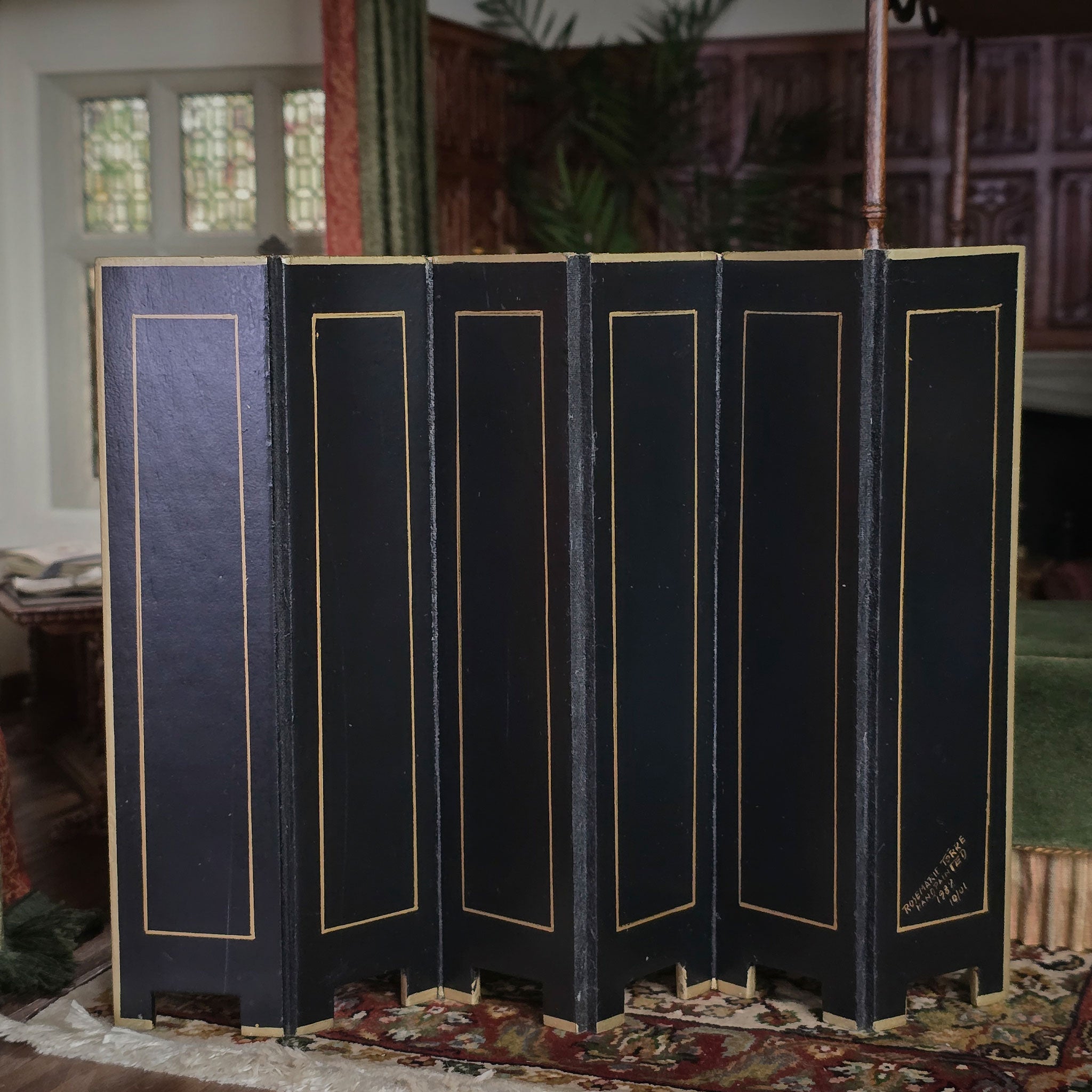 Black folding screen with gold trim in a room with stained glass windows and decorative rug.