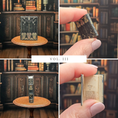 Load image into Gallery viewer, Collage of a miniature book with decorative cover and open pages, held by a hand in a library setting.

