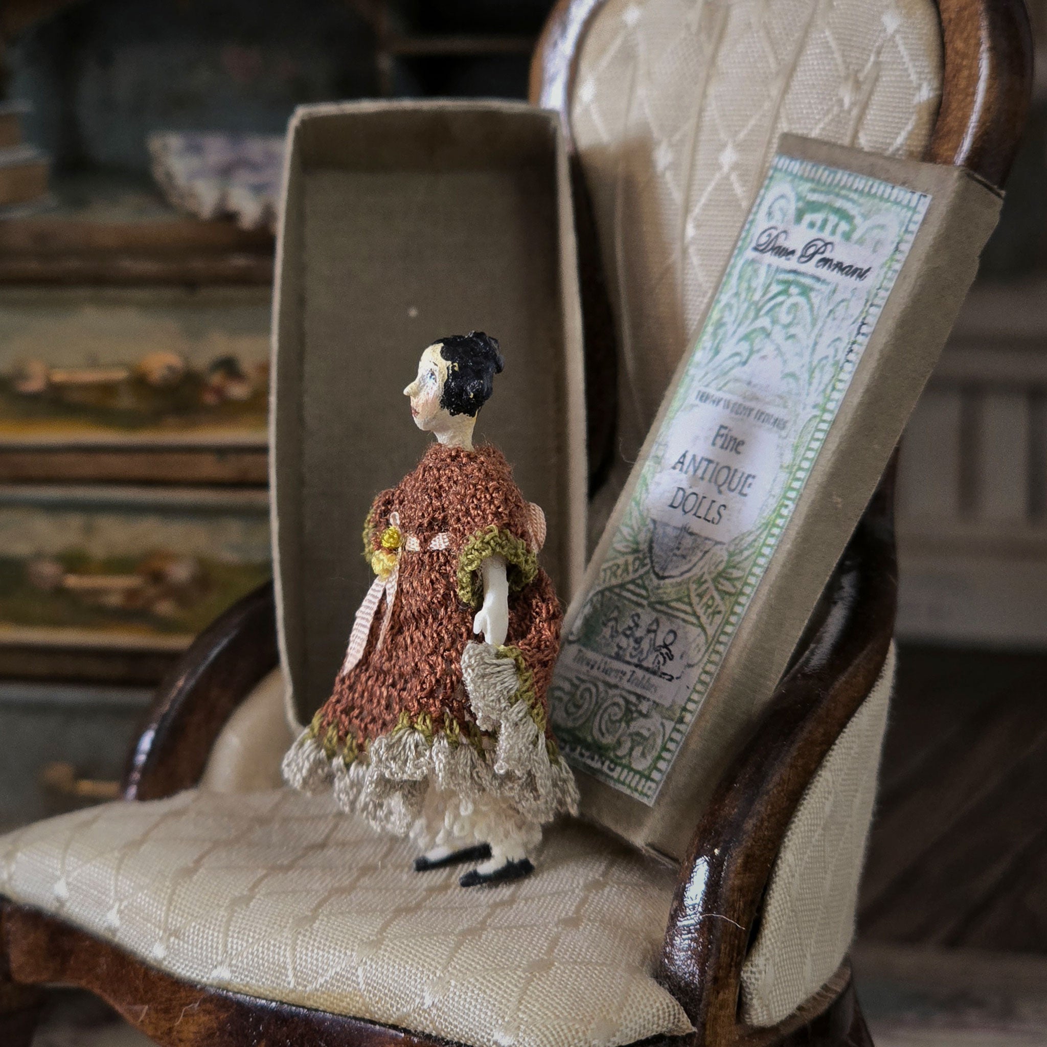 Small vintage-style doll on a chair with a label in the background