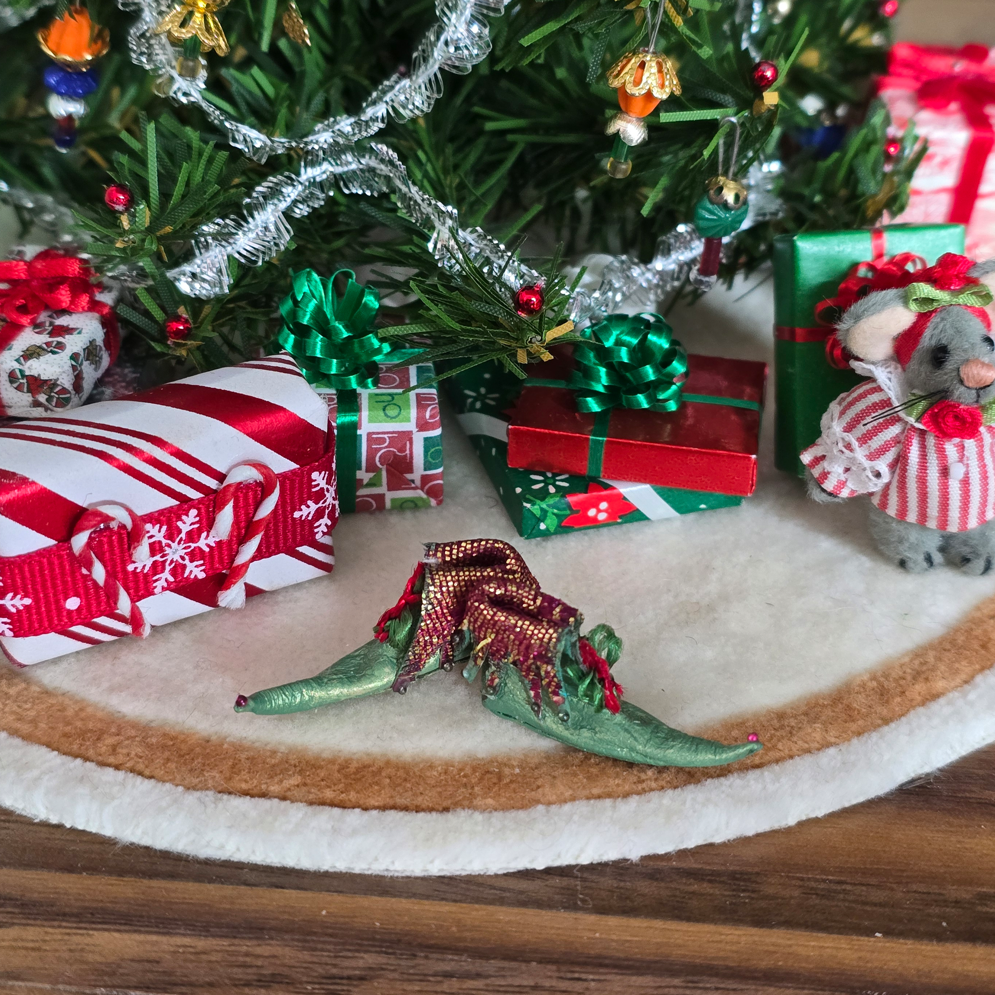 dollhouse miniature Christmas scene with small gifts, a tree, and festive pair of elves' shoes