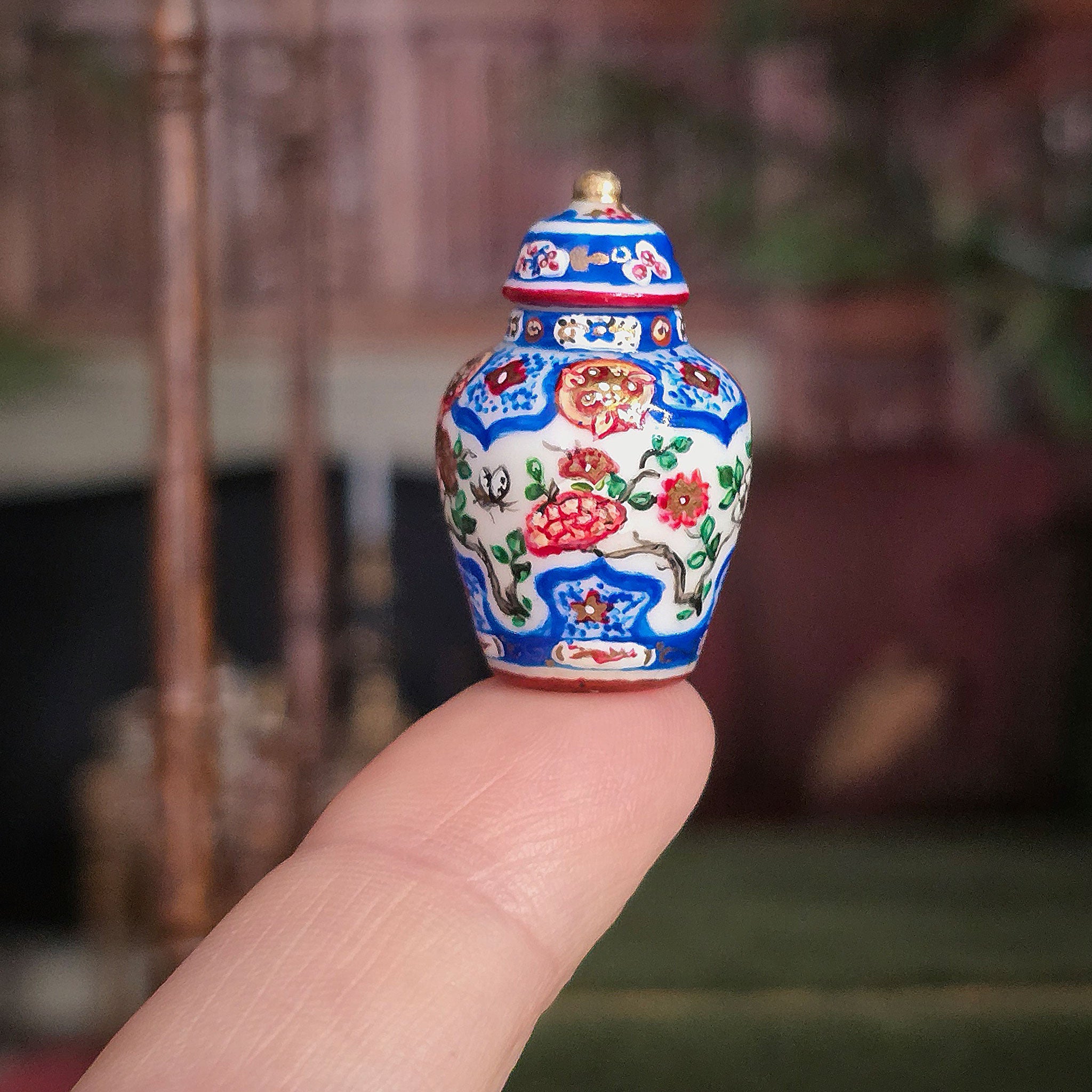 Small decorative vase with floral patterns held between fingers against a blurred background