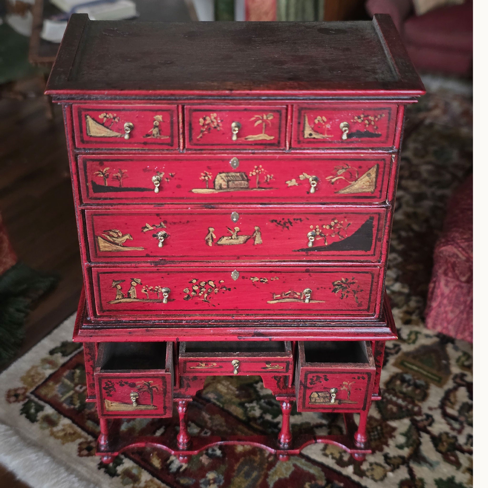 Red wooden chest of drawers with decorative carvings on a patterned rug. Alan Barnes