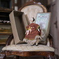 Load image into Gallery viewer, Small doll in a brown dress sitting on a vintage chair with a box in the background
