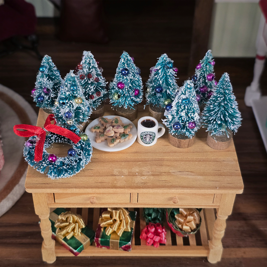 Decorative Christmas scene with miniature trees, wreath, and cookies on a wooden table.