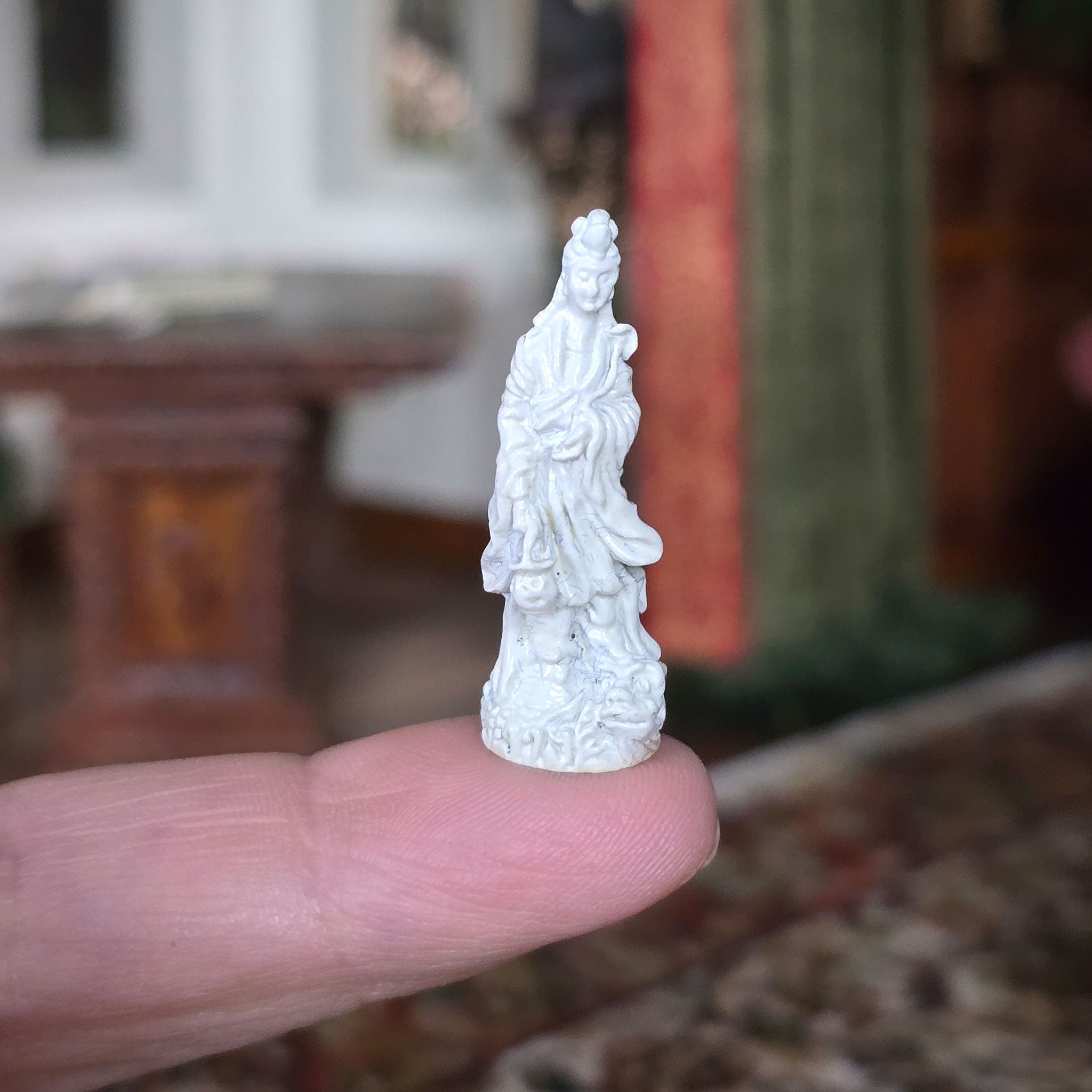 Small white statue held between fingers with a blurred background