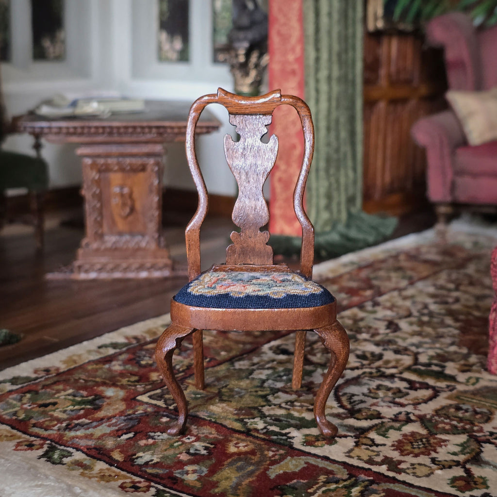 Wooden chair with a patterned needlepoint seat on a decorative rug in a room with furniture and decor.