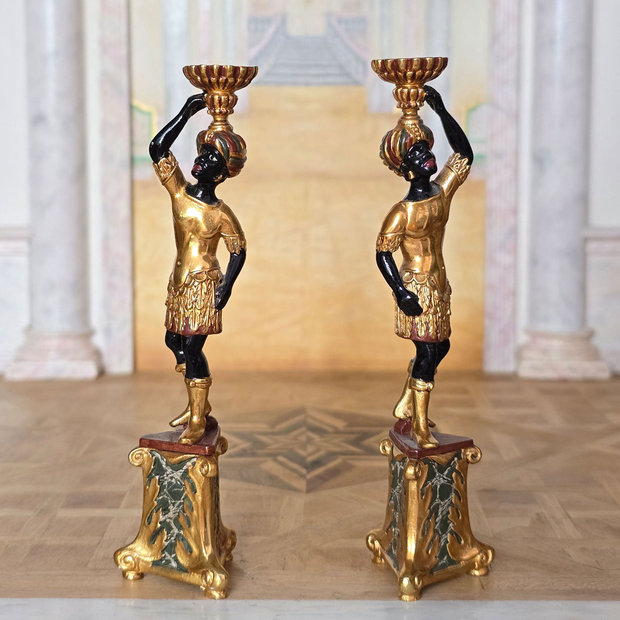 Pair of ornate pedestal stands with black and gold figures in a classical setting