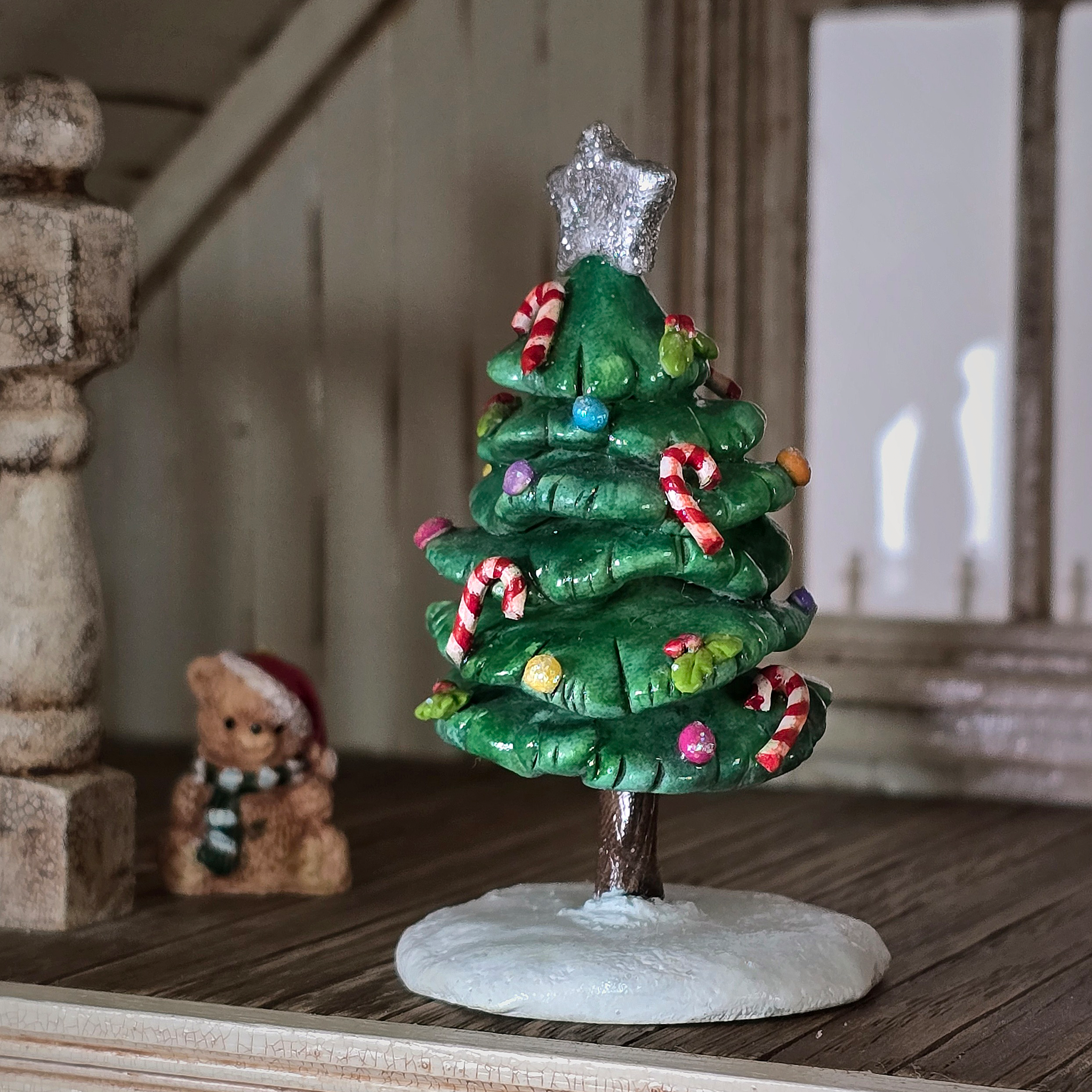Small decorative Christmas tree figurine with candy canes and a star on top, placed on a wooden surface.