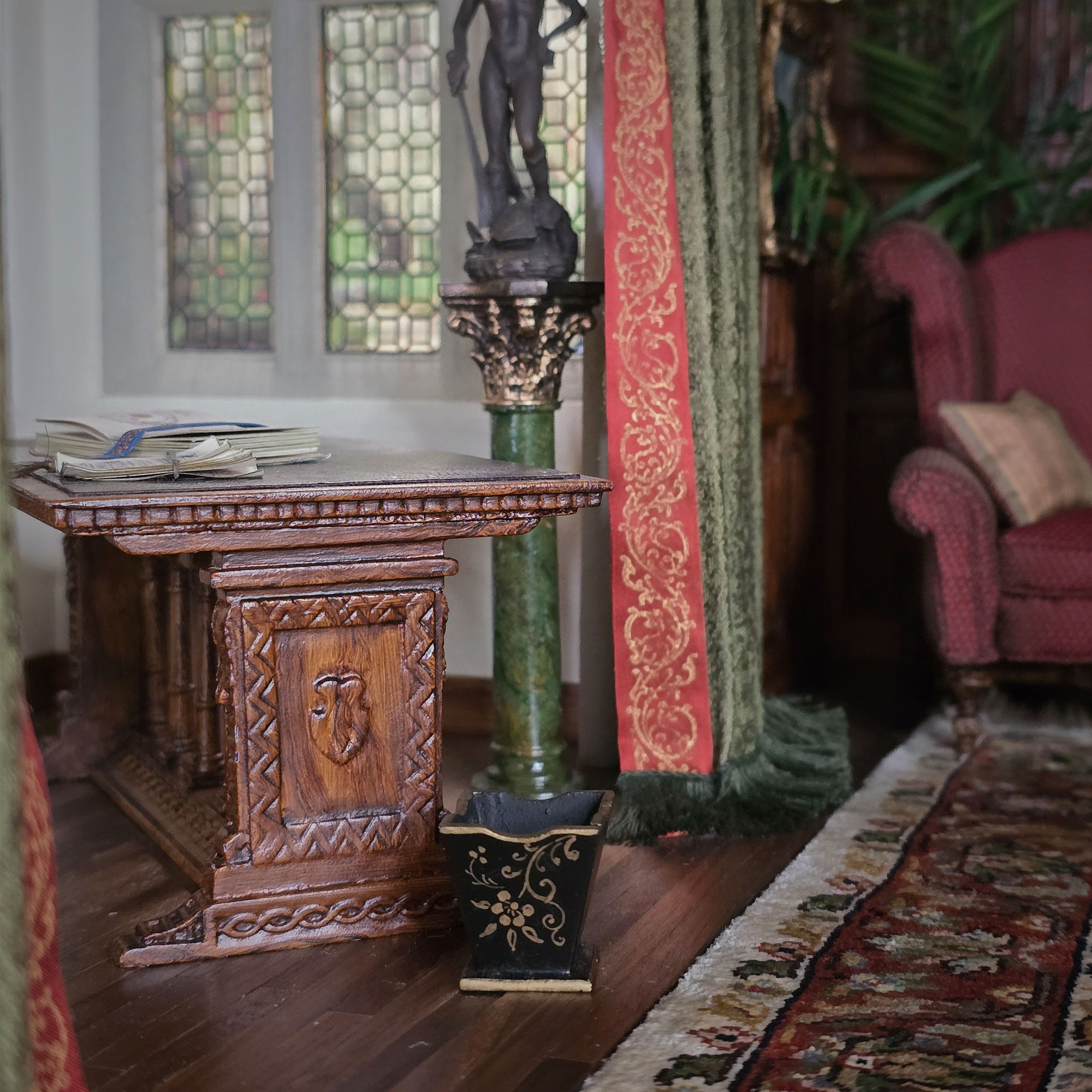Decorative interior setting with a wooden table, statue, and stained glass window and wooden waste bin.