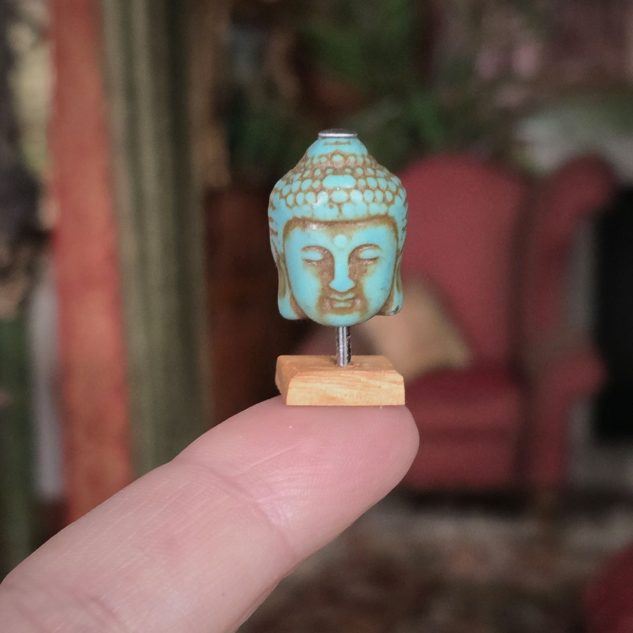 Small turquoise Buddha head on a wooden stand held by a hand with a blurred background