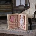 Load image into Gallery viewer, Small doll in a decorative box with heart patterns on a vintage-style lined background
