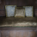 Load image into Gallery viewer, Three patterned pillows upon a cushion on a wooden bench against a wooden wall.
