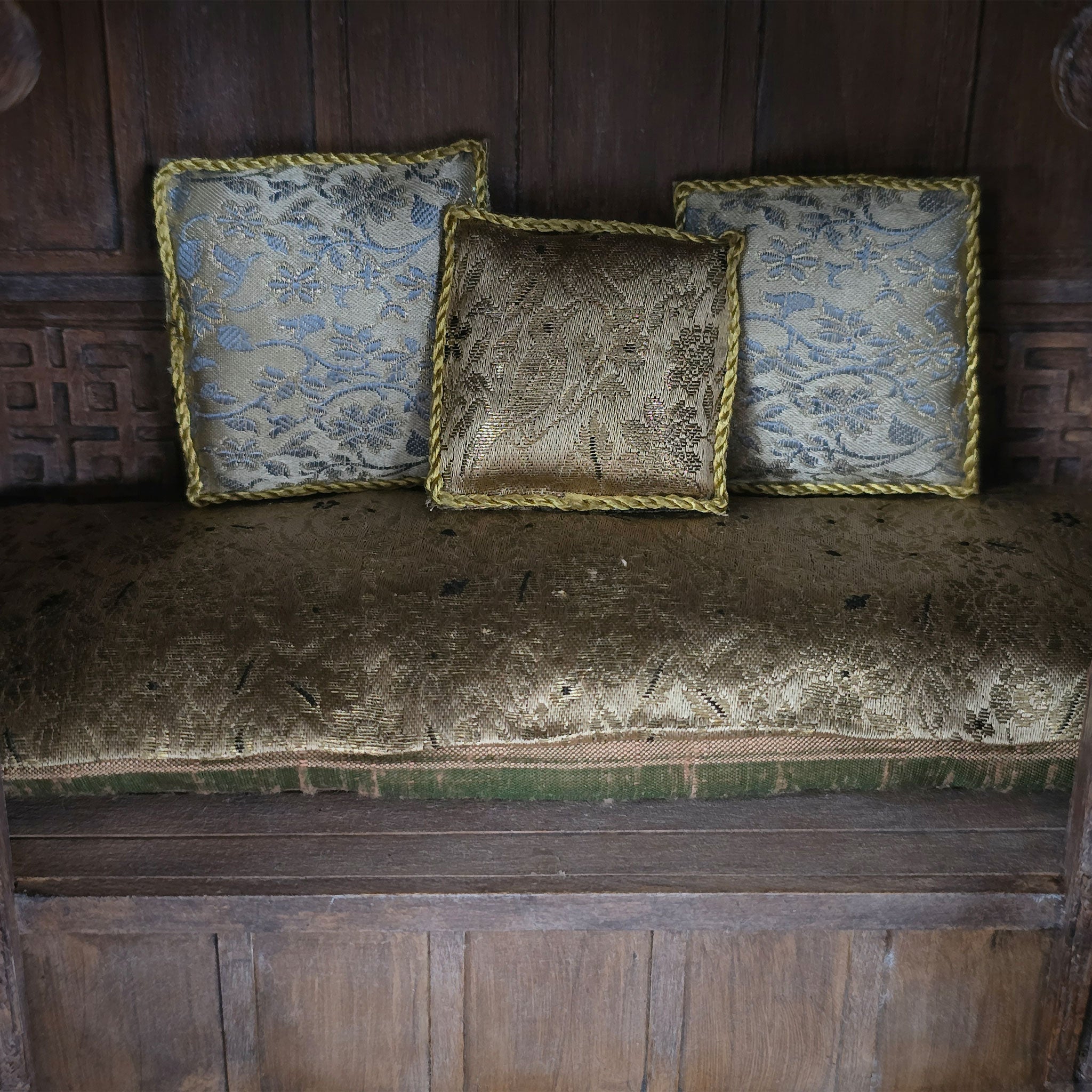 Three patterned pillows upon a cushion on a wooden bench against a wooden wall.