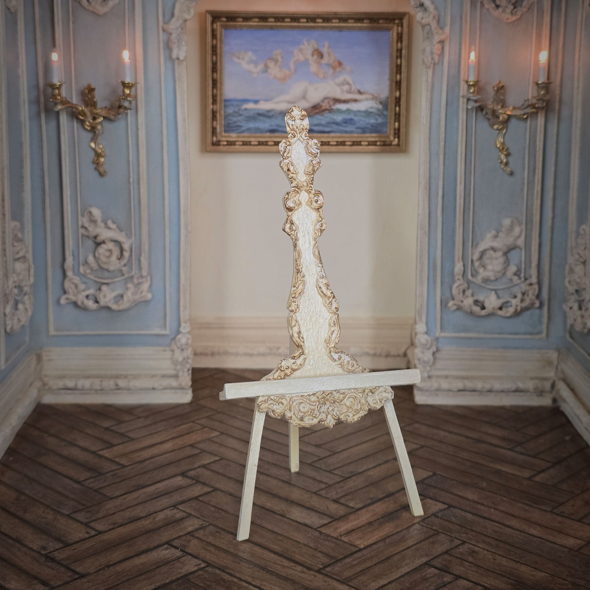 Decorative carved miniature easel in an ornate room with wall sconces and a painting.