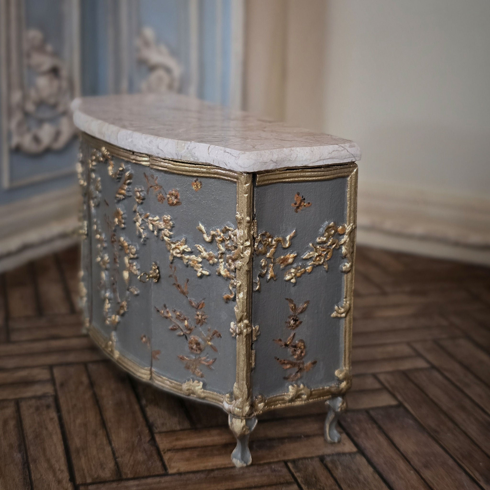 Decorative sideboard with marble top and gold leaf detailing in an ornate room.