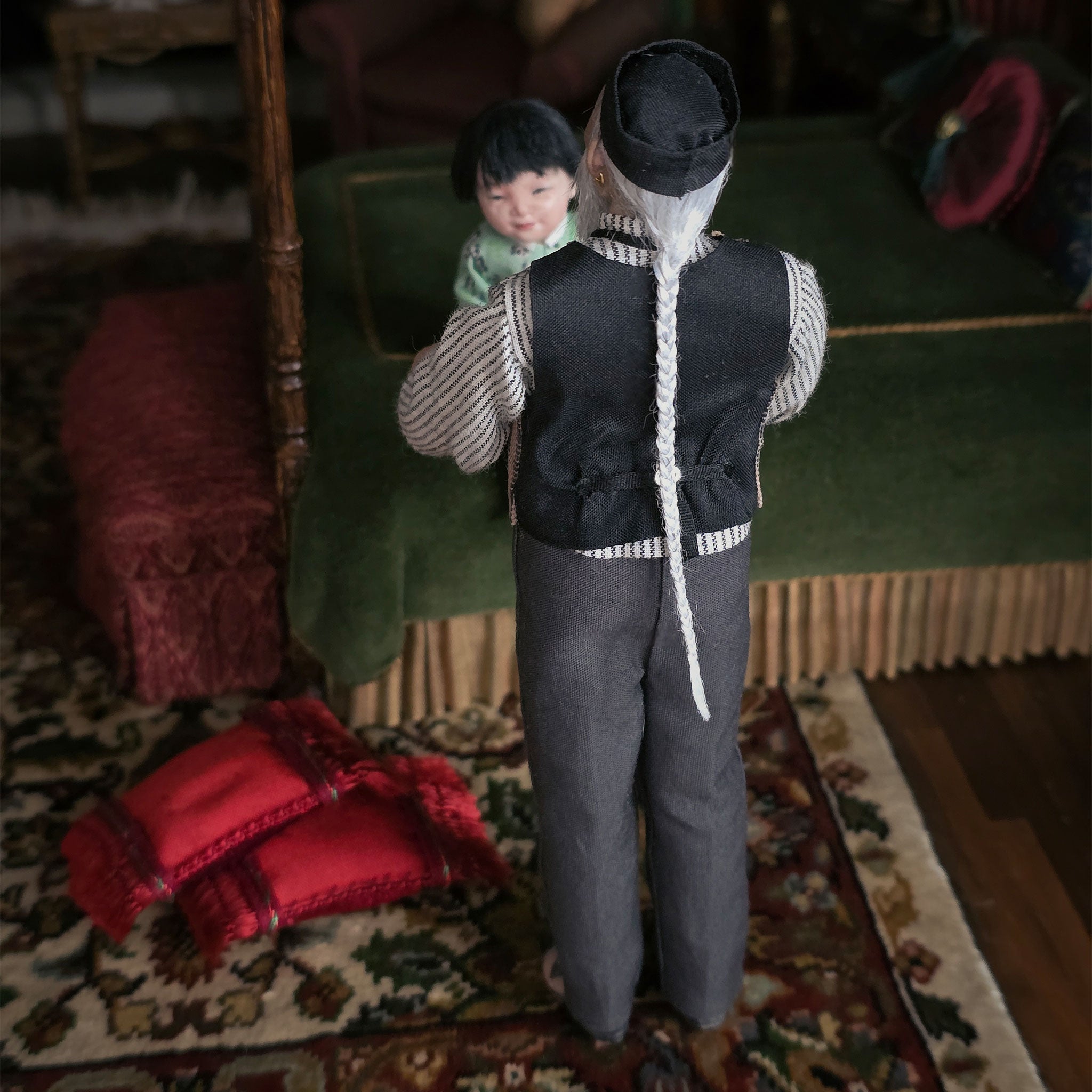 Dollhouse scene with a grandfather doll holding a child on a rug