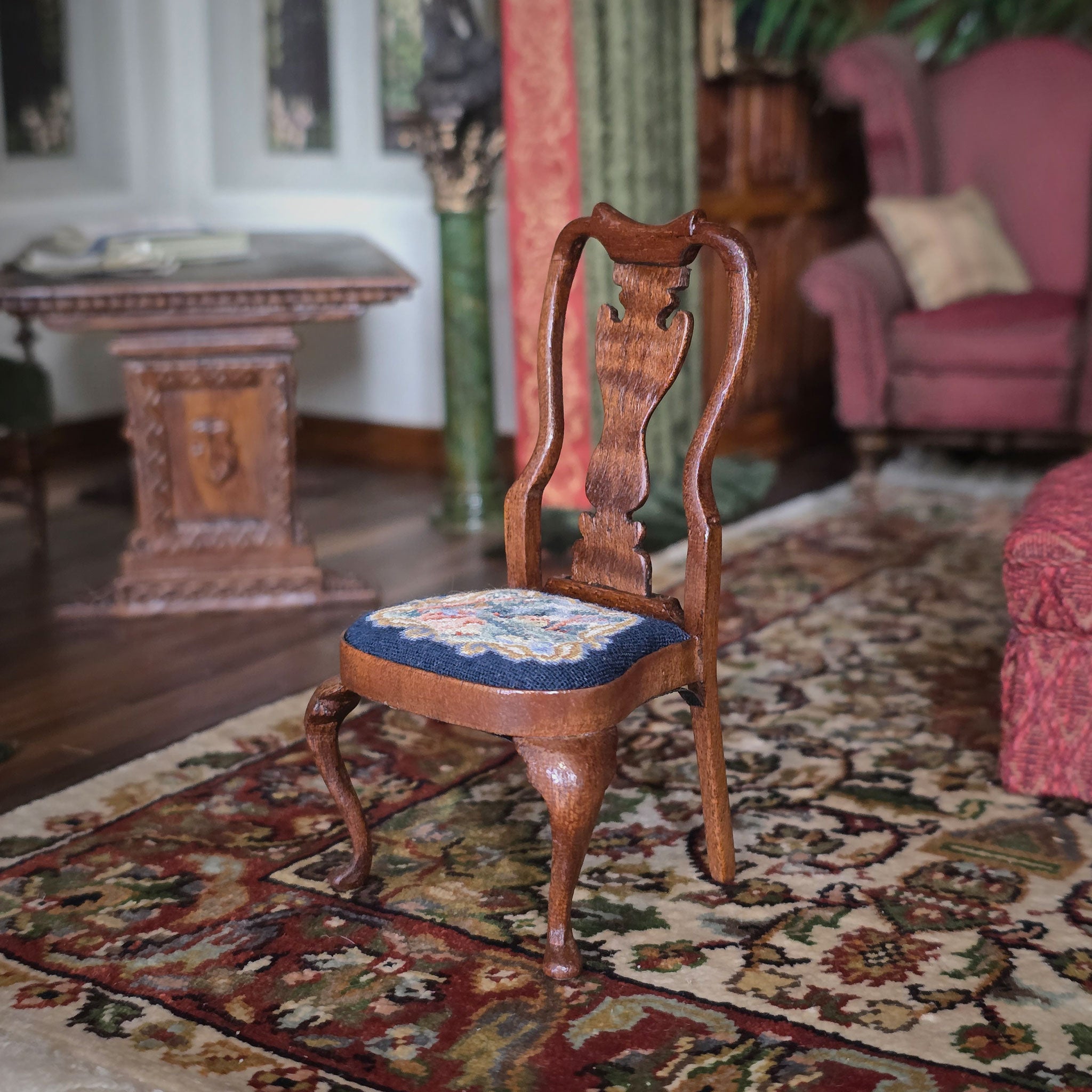 Wooden chair with a patterned petit point seat on a decorative rug in an elegant room.