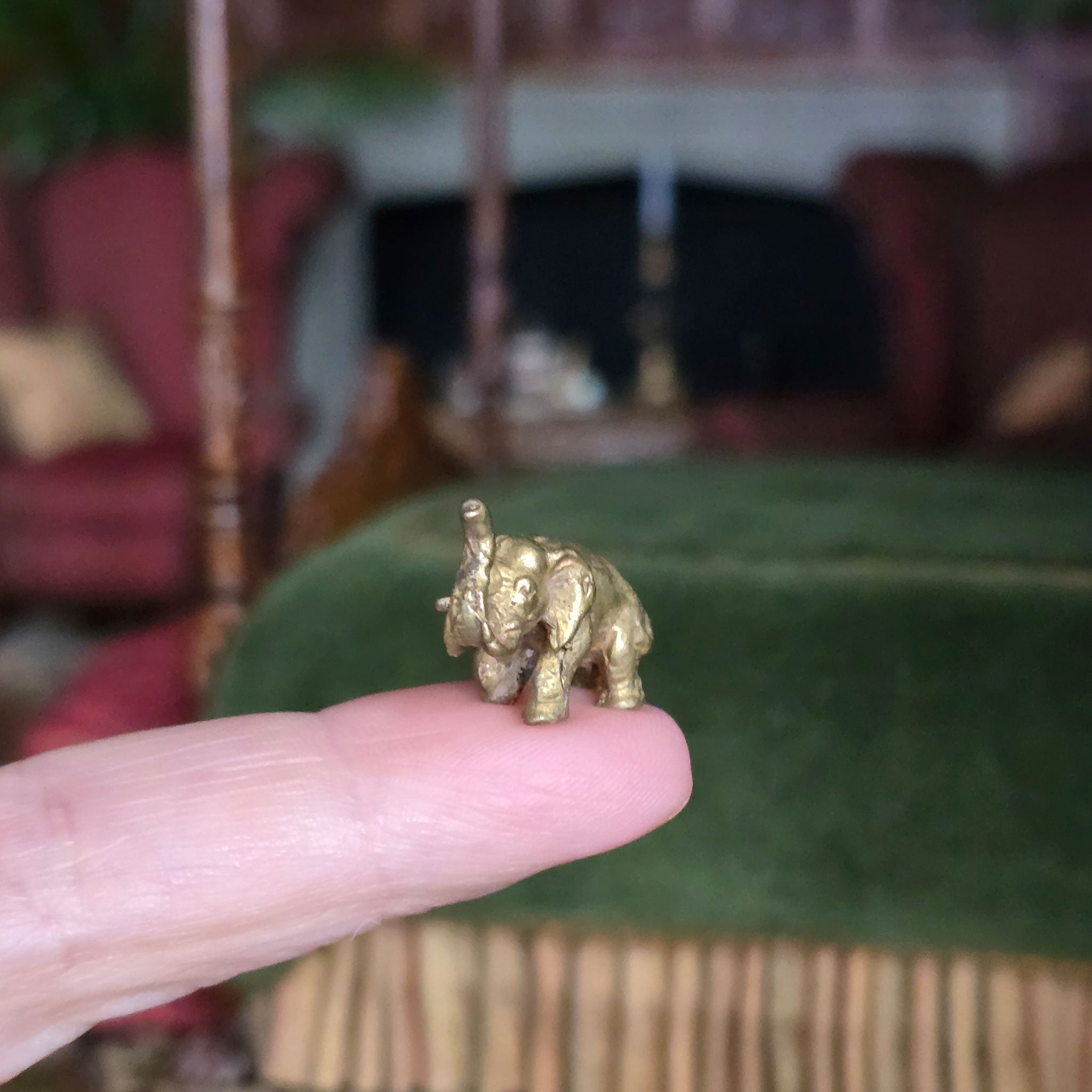 Gold elephant figurine held between fingers with a blurred indoor background