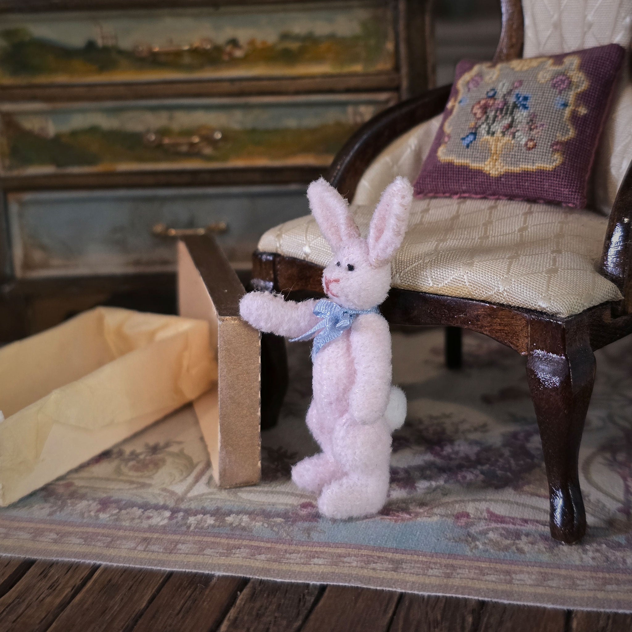 Pink stuffed bunny with a blue bow standing on a patterned rug next to an antique wooden chair.