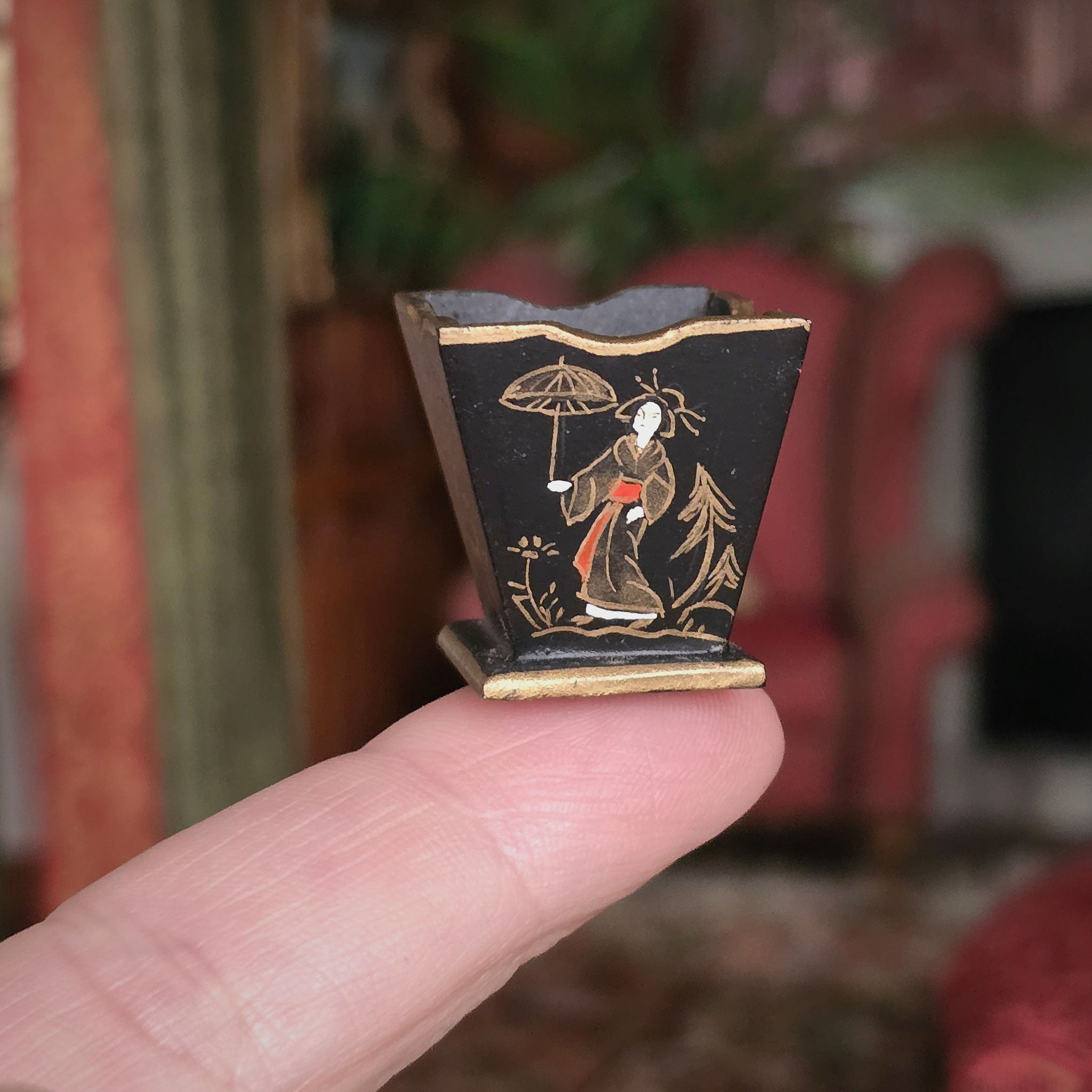 Small decorative waste bin with a person holding it on a finger against a blurred background.