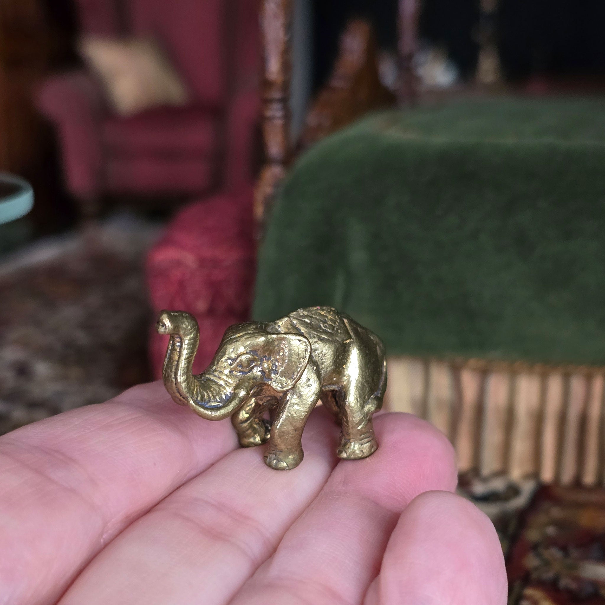 Small gold elephant figurine held in a hand with a blurred indoor background