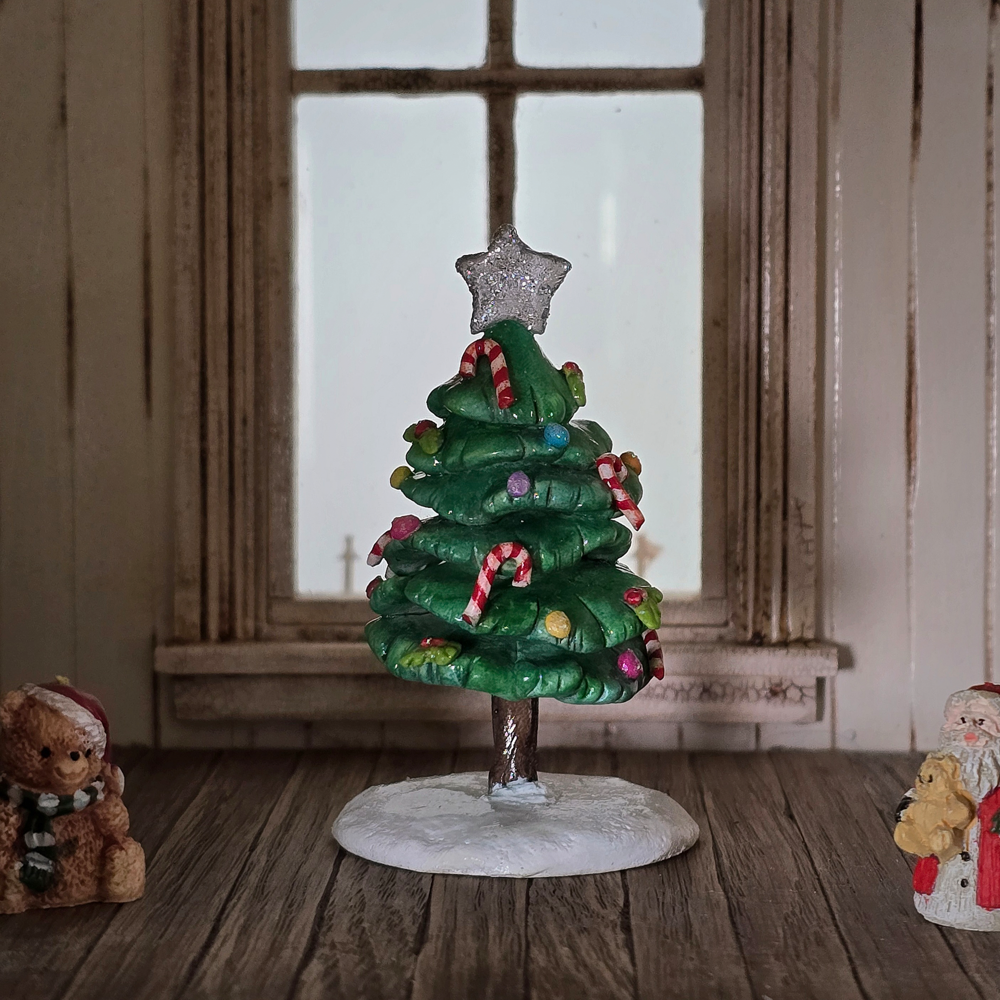 Decorative Christmas tree figurine with a star on top, surrounded by small teddy bears, in a room with wooden floor and window.