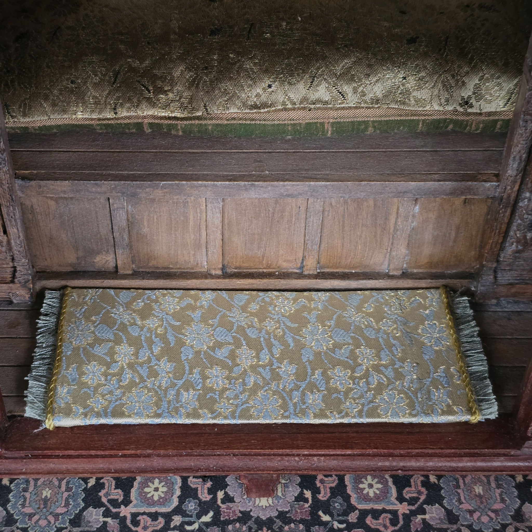 Decorative silk rug with intricate patterns on a wooden bench of alcove bed