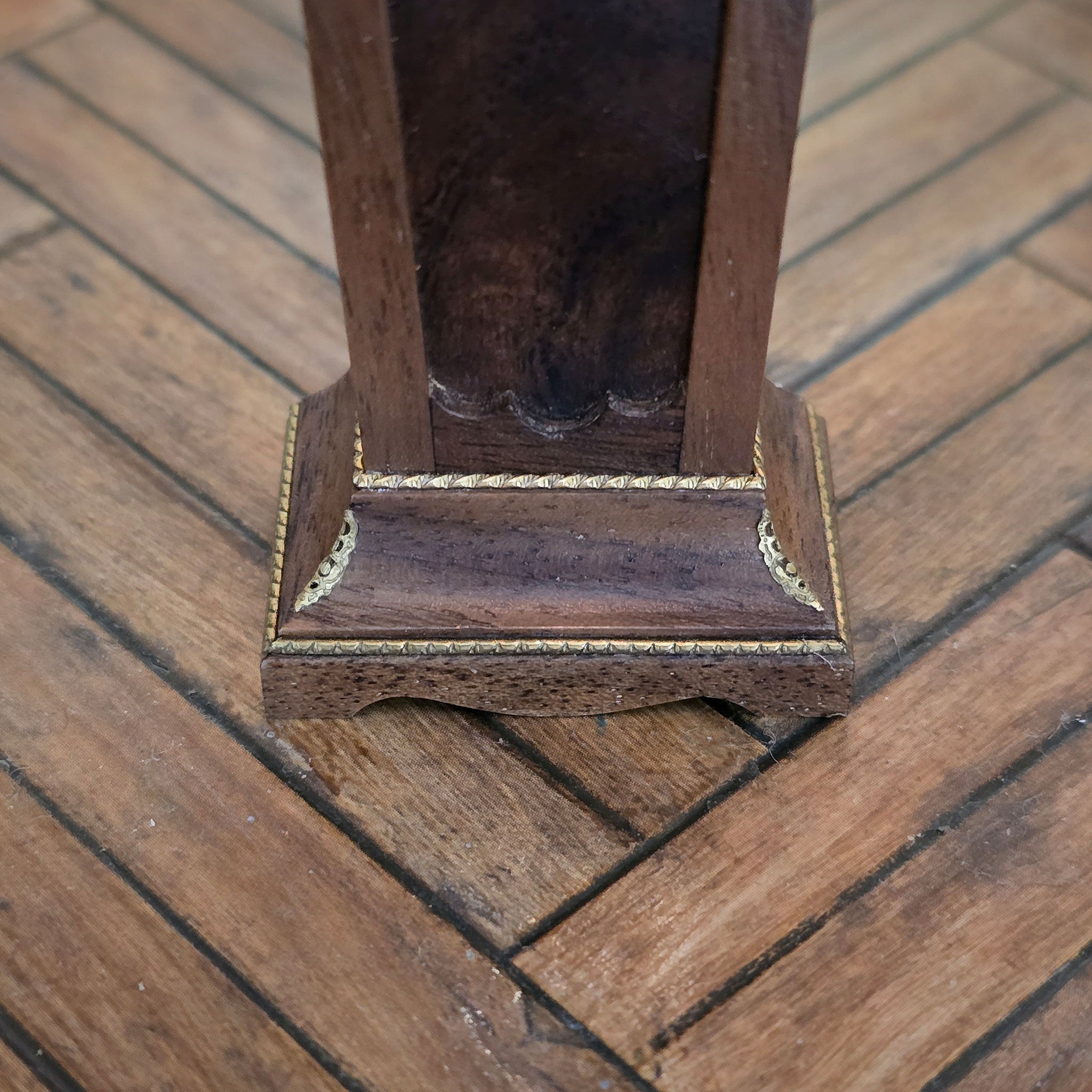 Close-up of a wooden pedestal with decorative trim on a wooden floor.