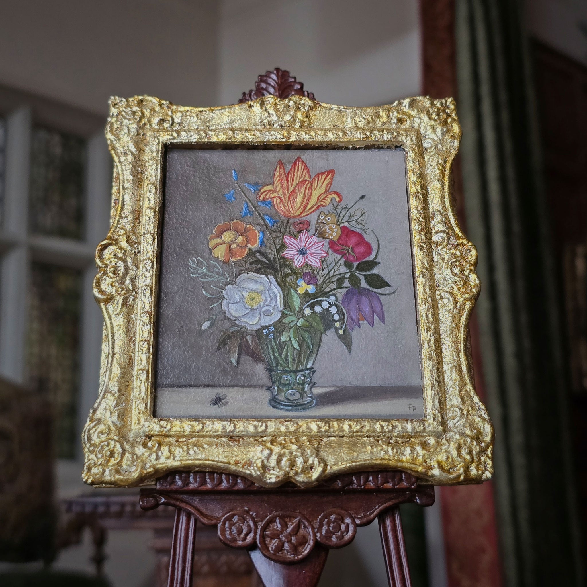 Decorative painting in miniature of a floral arrangement in a gold frame on an easel.